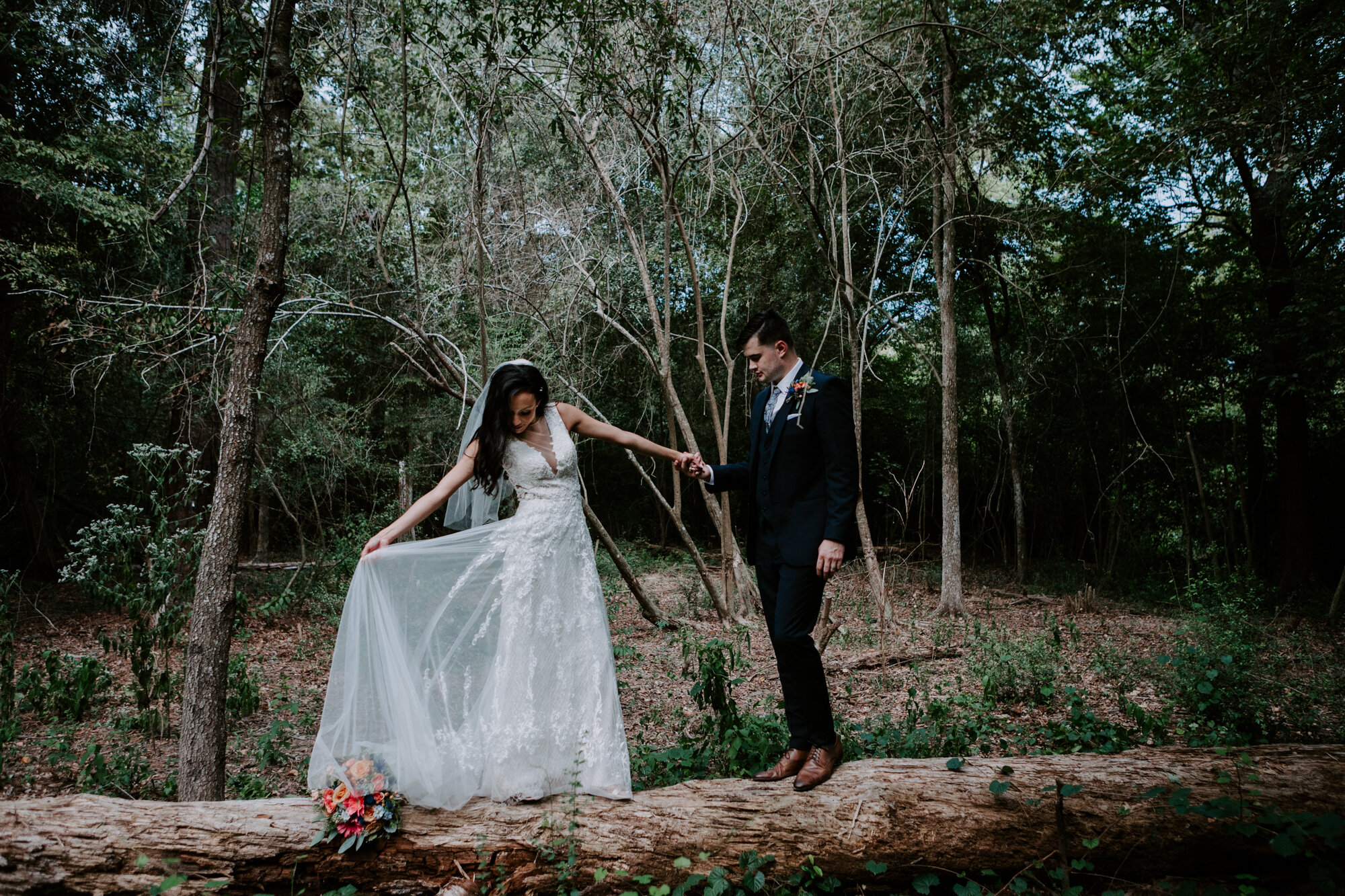 Bride holding her train on a fallen tree. Vivacious Wedding at Houston Arboretum and Nature Center