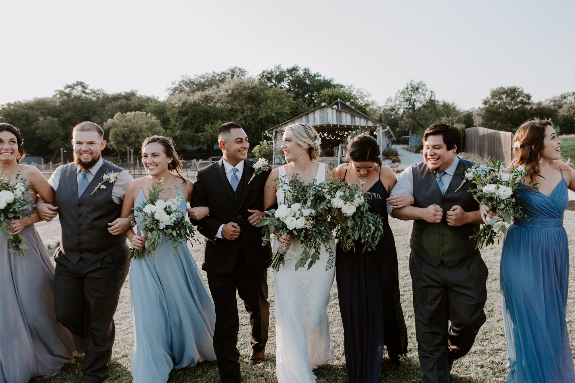 Bride and groom walking laughing with bridal party. Radiant Bohemian Hill Country Wedding at Gruene Estate in New Braunfels, TX