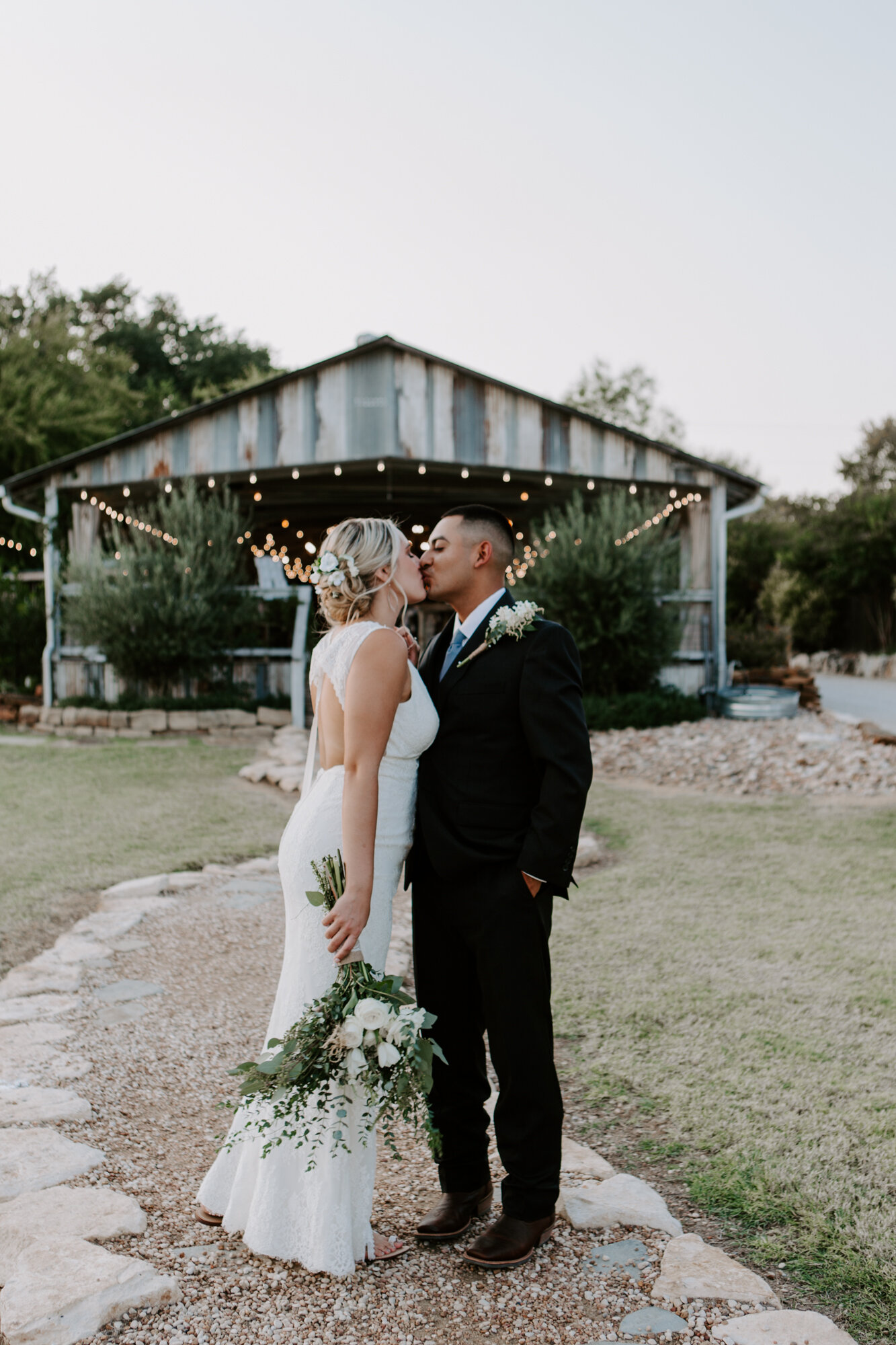 Bride and groom kiss in front of the venue in sunset. Radiant Bohemian Hill Country Wedding at Gruene Estate in New Braunfels, TX