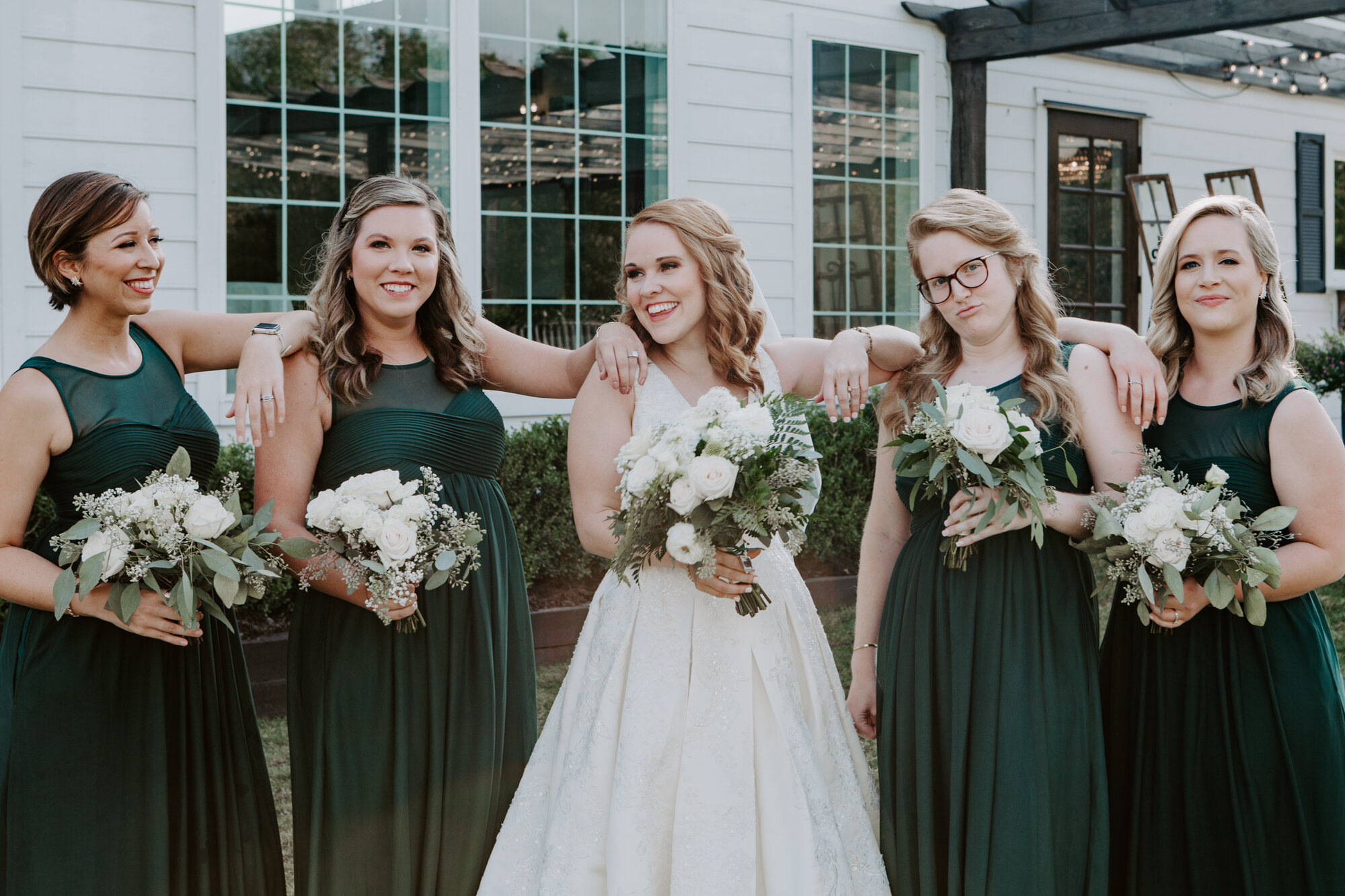 Bride and bridesmaids portraits smiling looking at each other. Mesmerizing Wedding in Emerald Green at Venue 311 in Plantersville, TX 