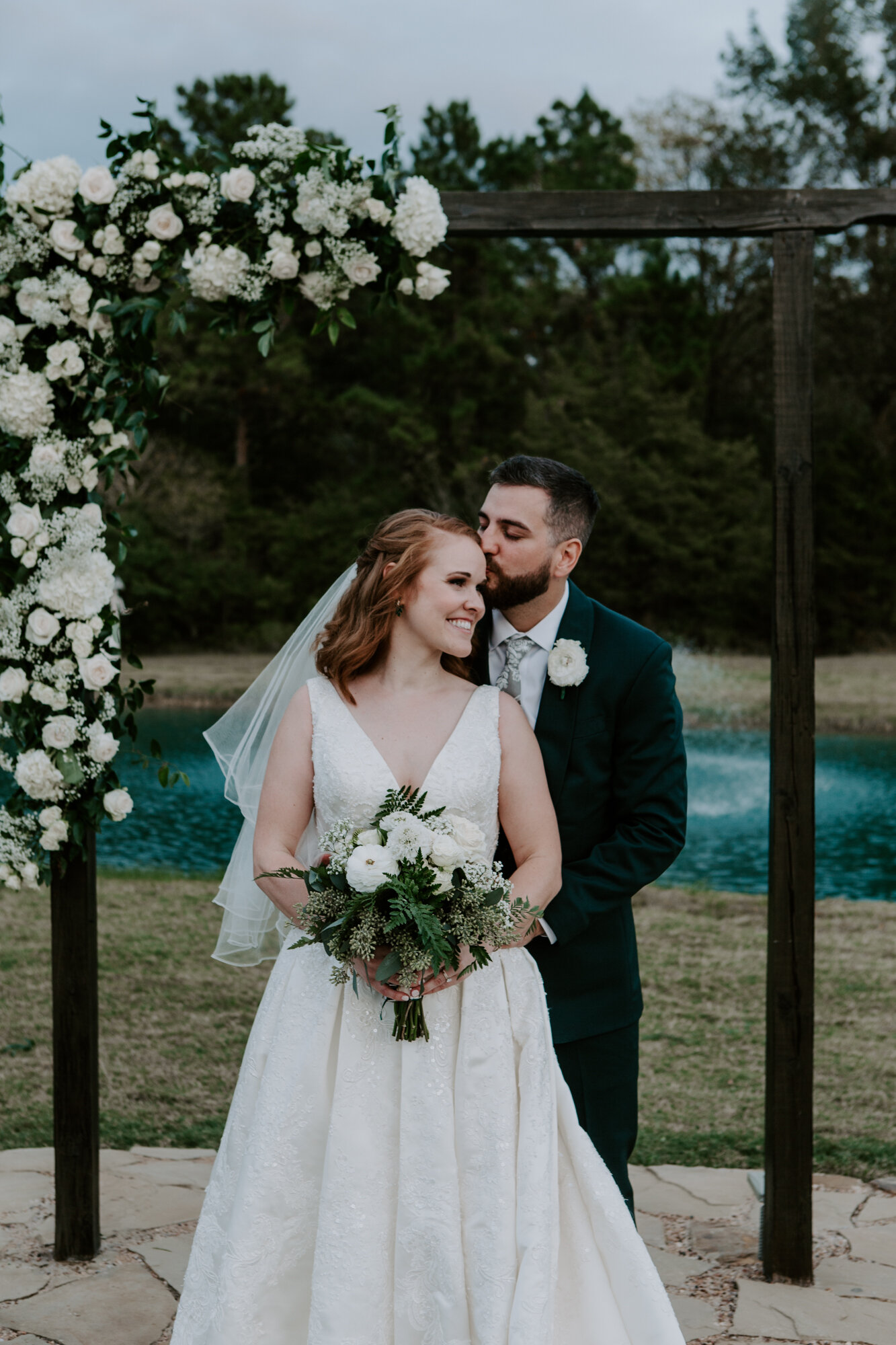 Bride and groom portrait by the floral arch. Mesmerizing Wedding in Emerald Green at Venue 311 in Plantersville, TX 