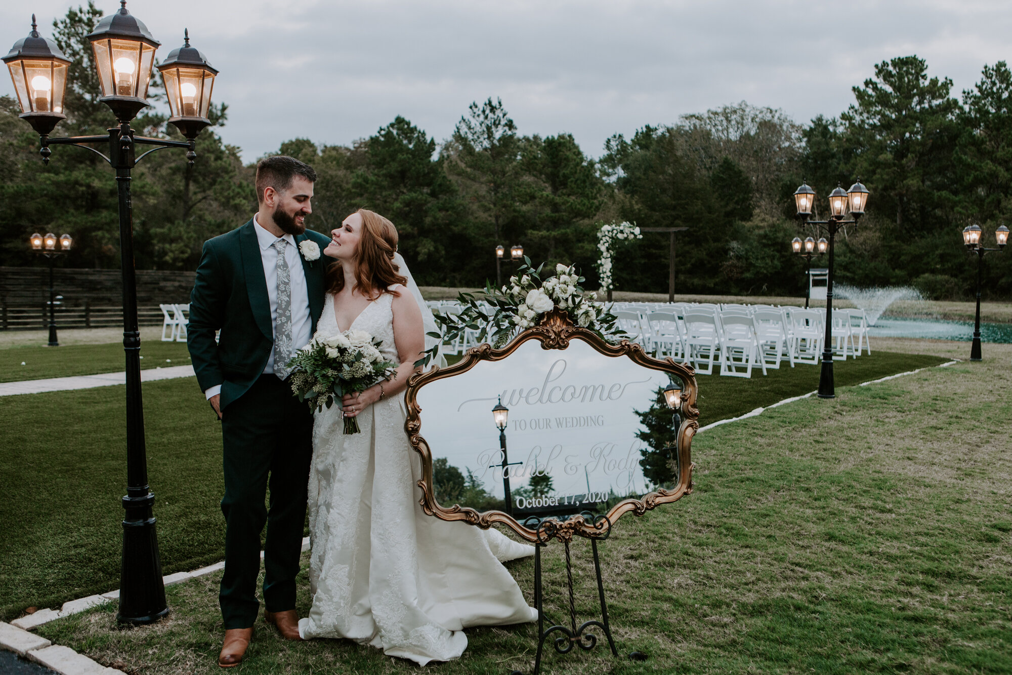 Bride and groom by the wedding sign. Mesmerizing Wedding in Emerald Green at Venue 311 in Plantersville, TX