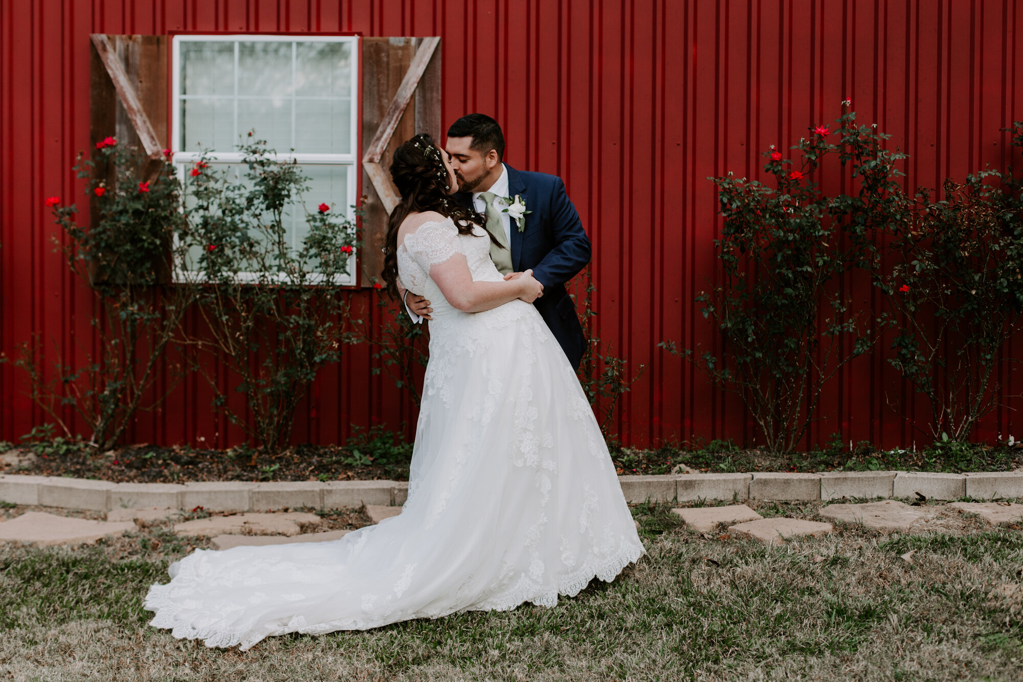 Bride and groom kissing by the red wall. Fairy Romantic Wedding at Magnolia Bells in Magnolia, TX