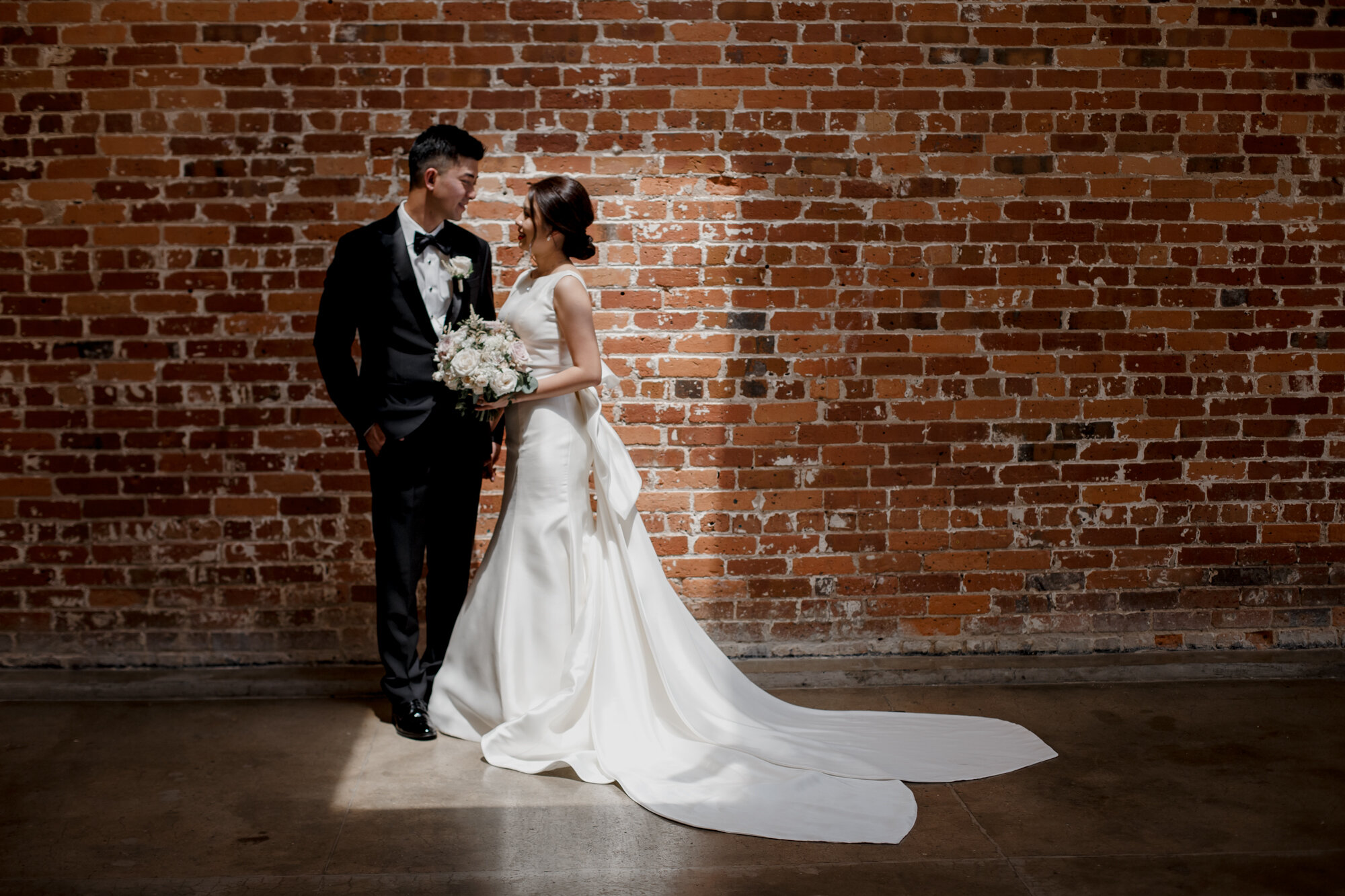Bride and groom by the brick wall in the sunlight. Urban Elegant East Asian Wedding at Ronin 2