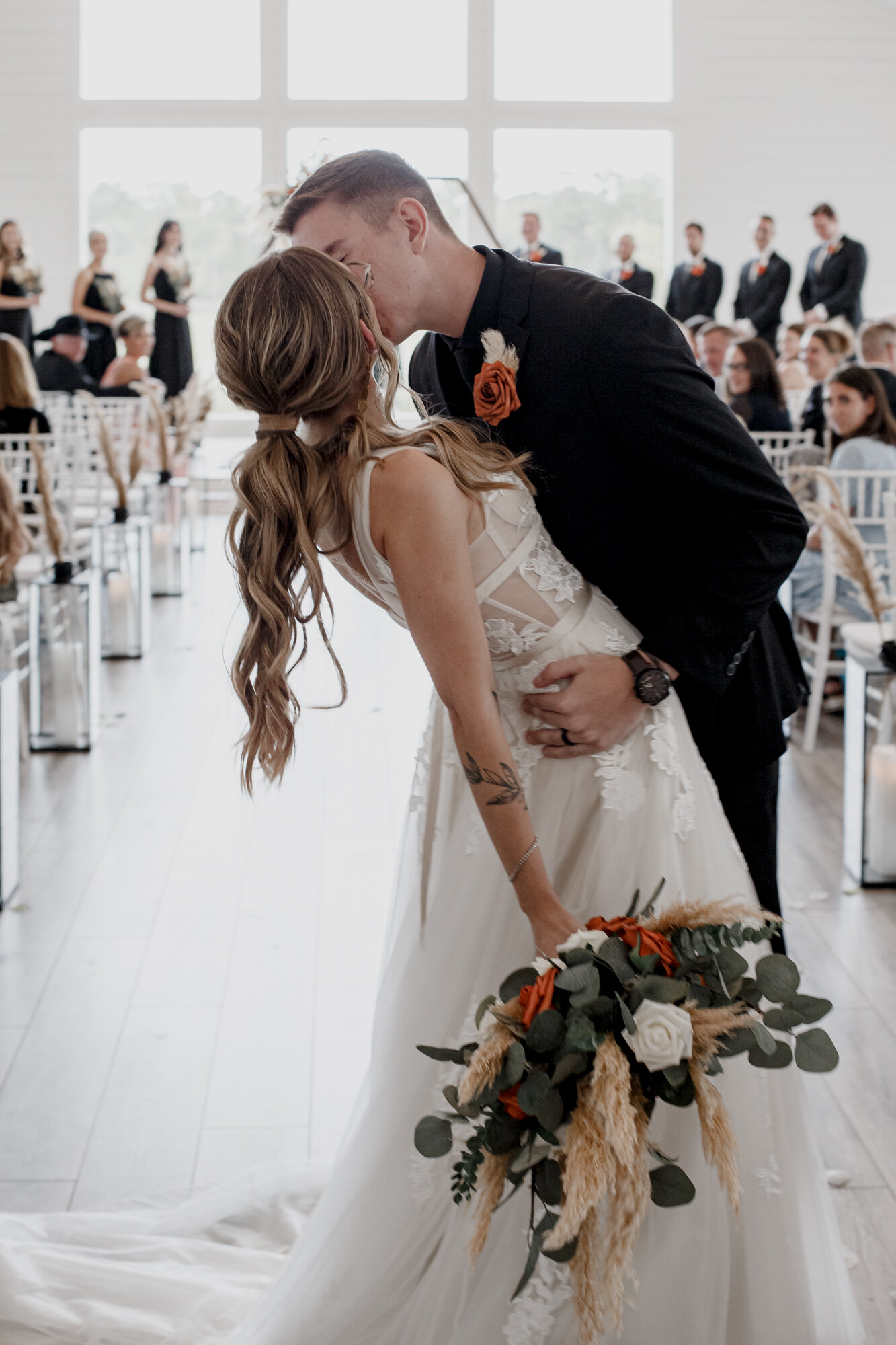 Bride and groom kiss on the aisle. Burnt Orange and Black Fall Wedding at The Farmhouse