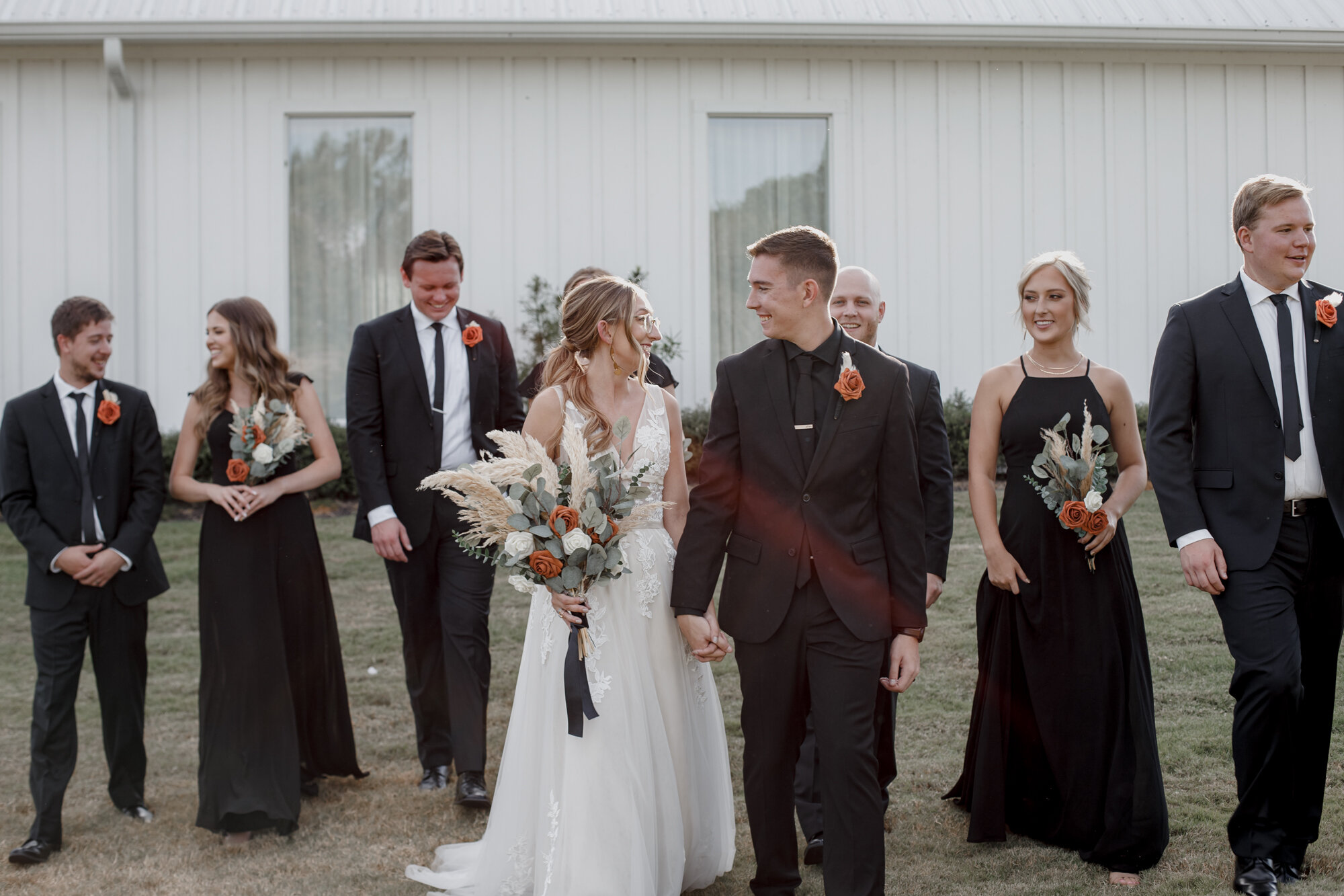 Bride and groom walk together with bridal party. Burnt Orange and Black Fall Wedding at The Farmhouse