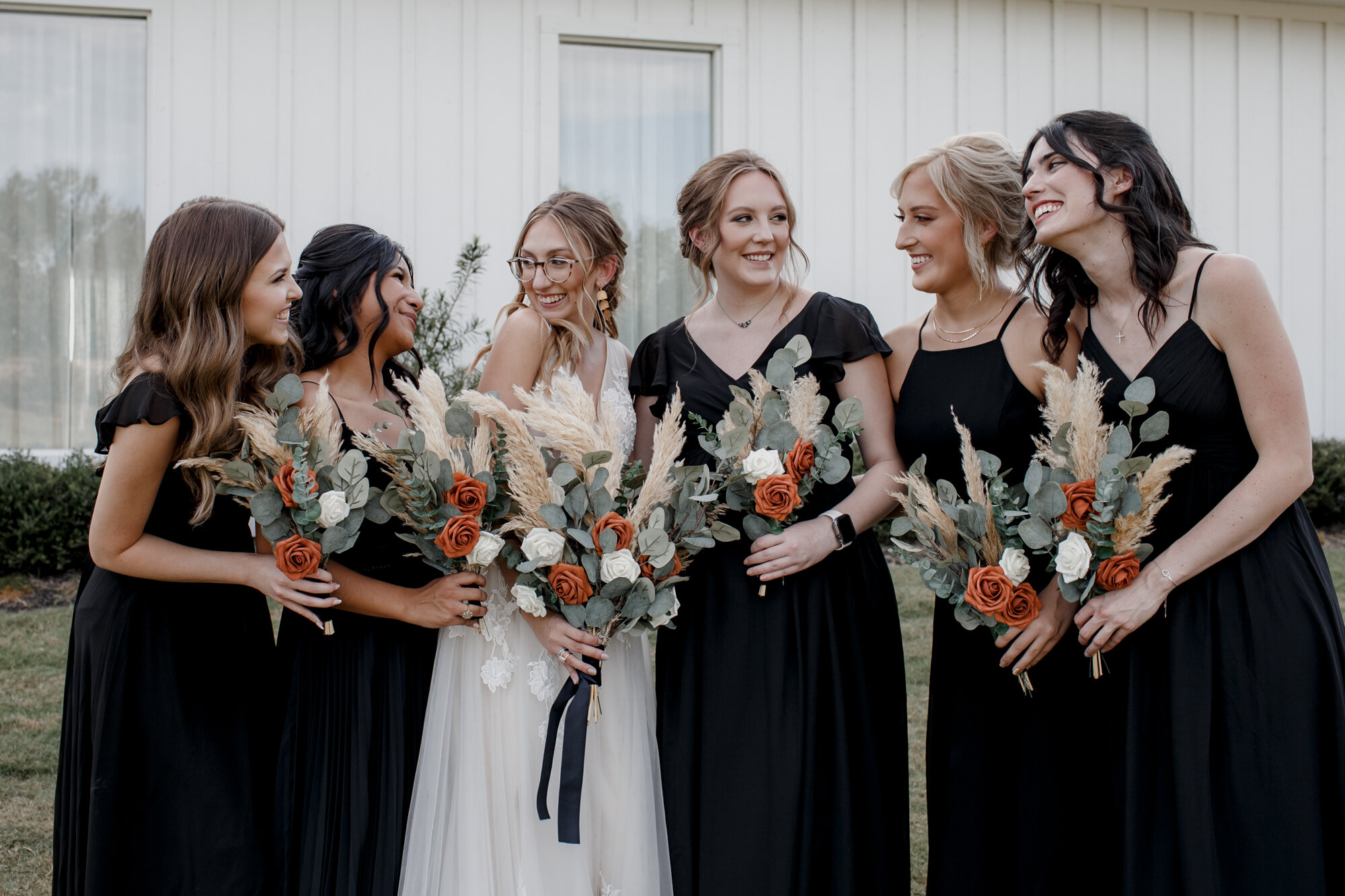 Bride and bridesmaids looking at each other. Burnt Orange and Black Fall Wedding at The Farmhouse