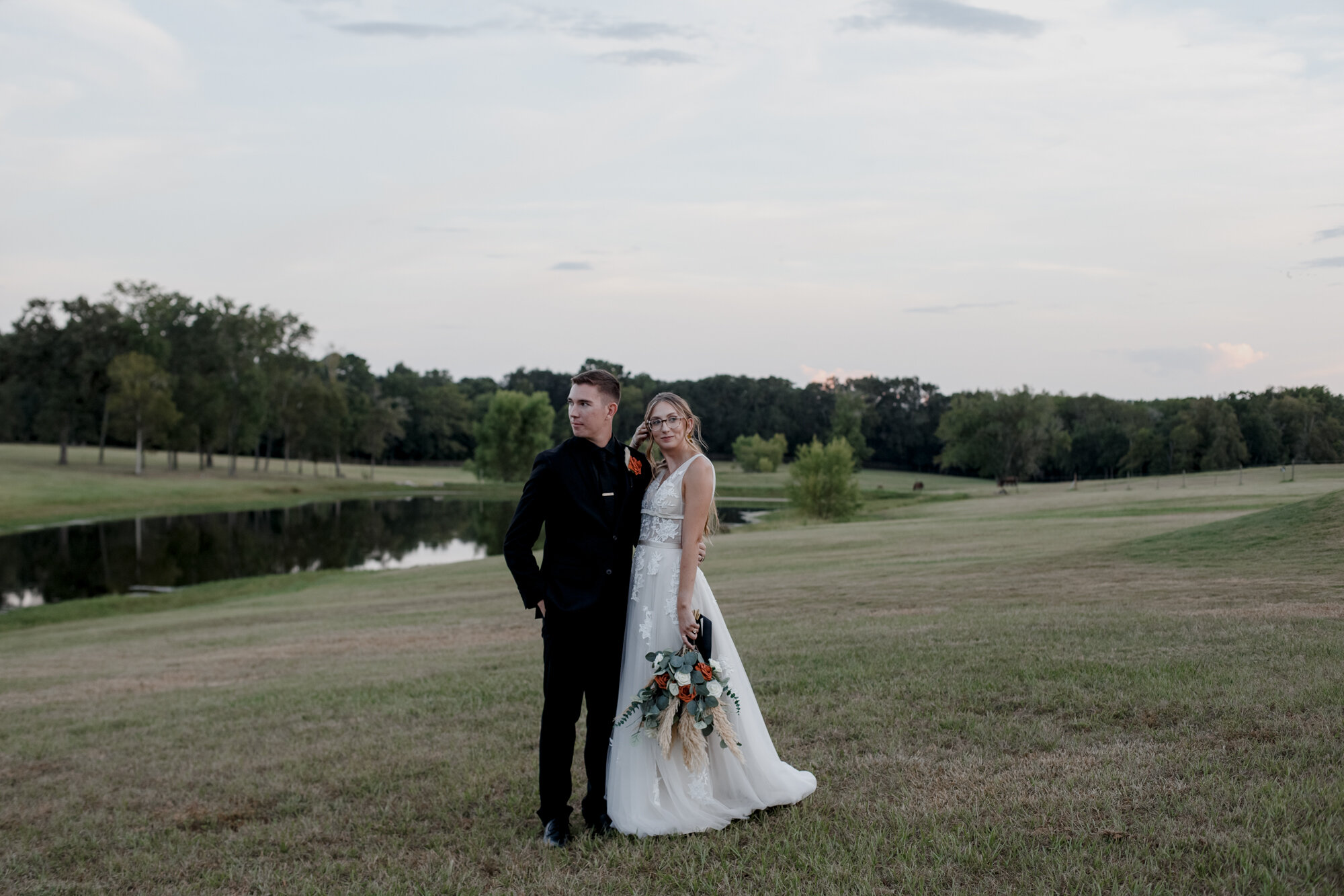 Bride and groom pose in the field. Burnt Orange and Black Fall Wedding at The Farmhouse