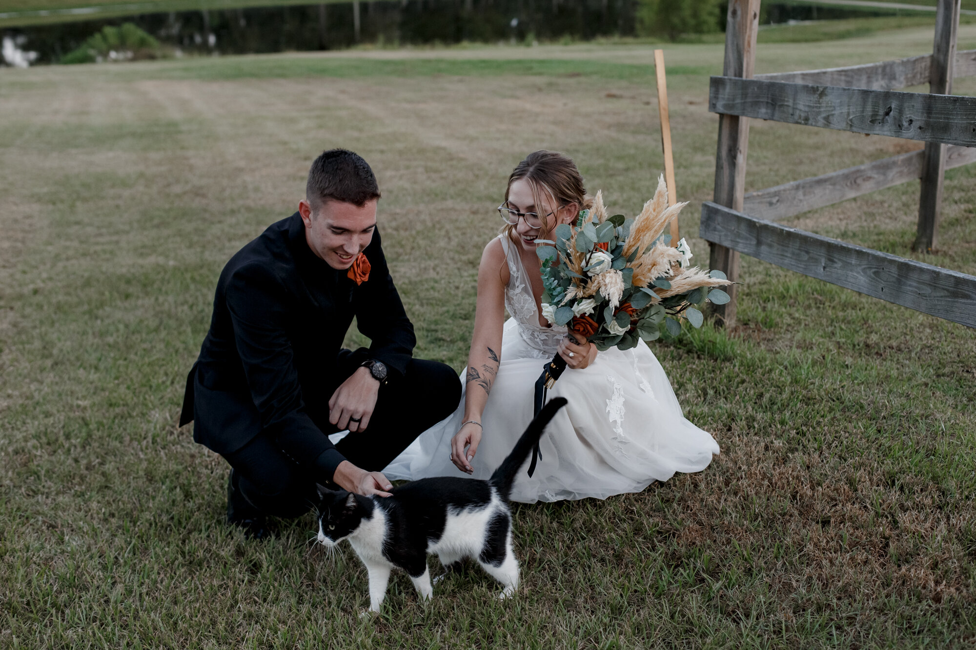 Bride and groom play with a cat. Burnt Orange and Black Fall Wedding at The Farmhouse