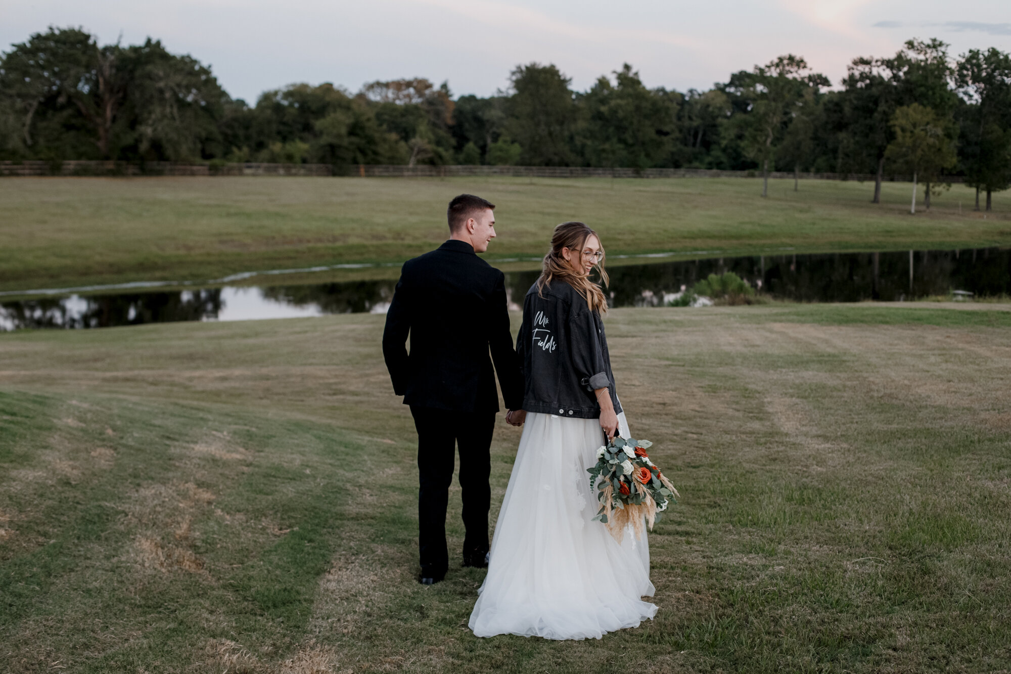 Bride and groom walk away holding hands. Burnt Orange and Black Fall Wedding at The Farmhouse