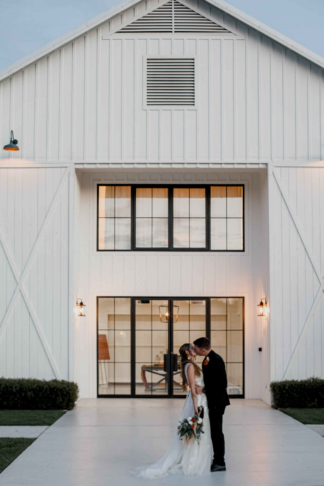 Bride and groom kissing by the venue sunset portraits. Burnt Orange and Black Fall Wedding at The Farmhouse