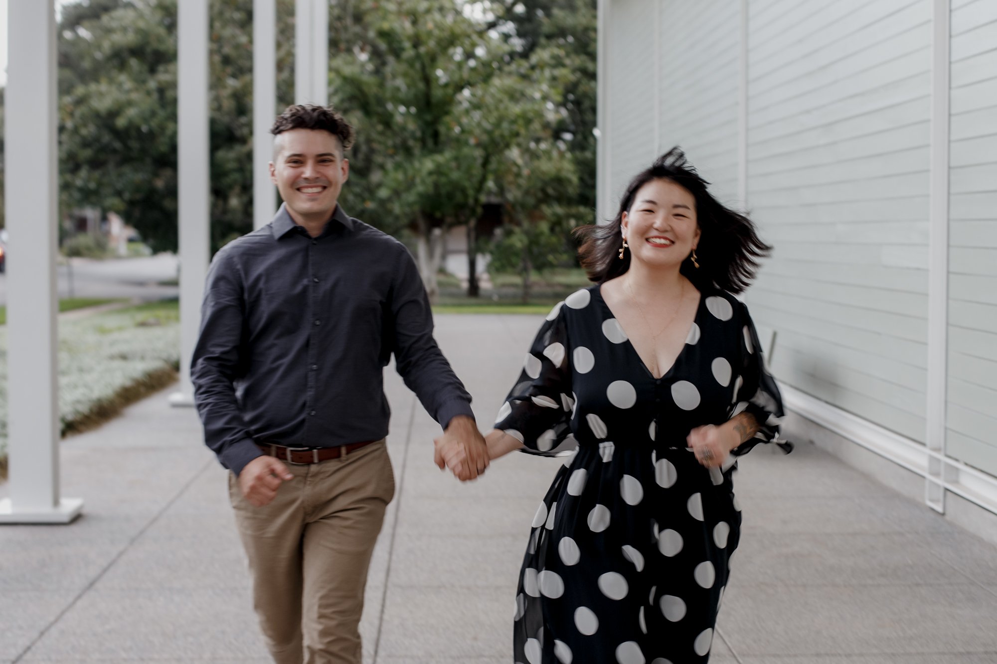 Couple runs holding hands - Stylish Polka Dot Dress Engagement Photo Session at Menil Park