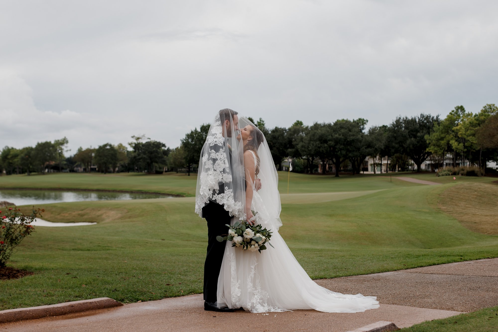 Bride and groom under veil kiss. Wedding at Royal Oaks Country Club