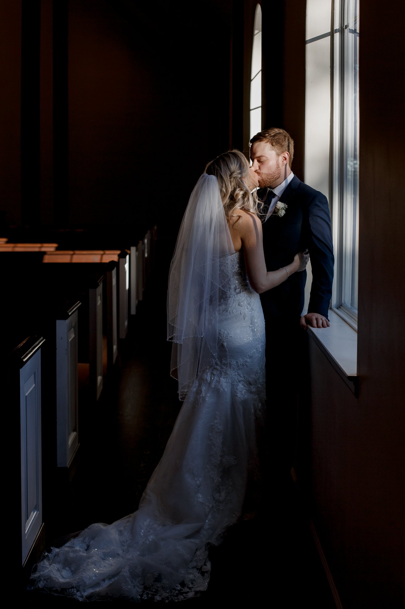 Bride and groom kissing - dramatic portrait in the chapel by the window. Wedding at The Vine (New Ulm, TX)