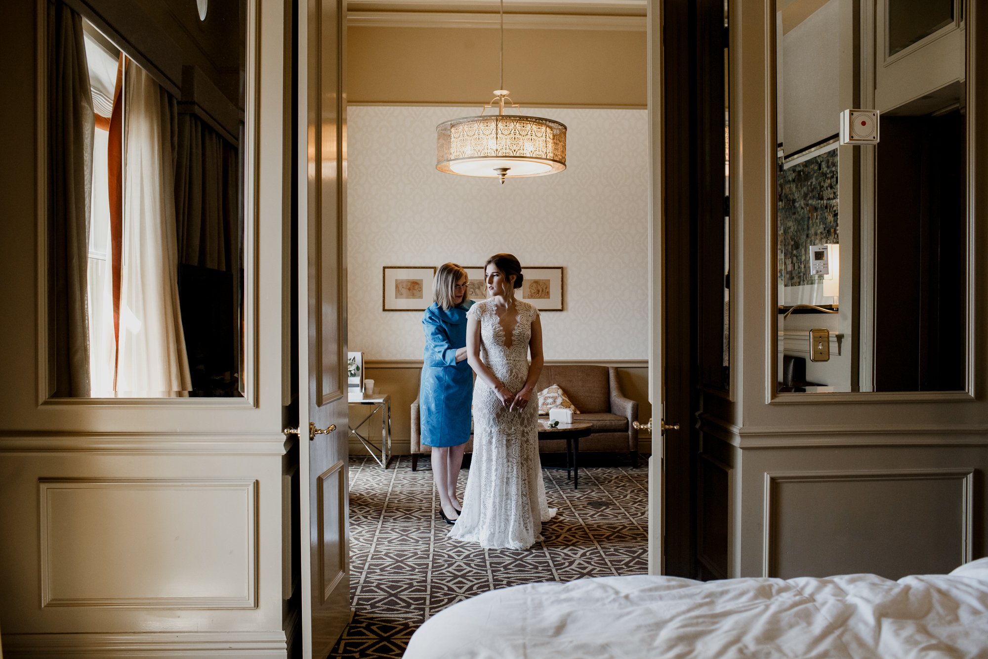 Mother zipping bride's dress with the room view. Wedding at Hotel Icon