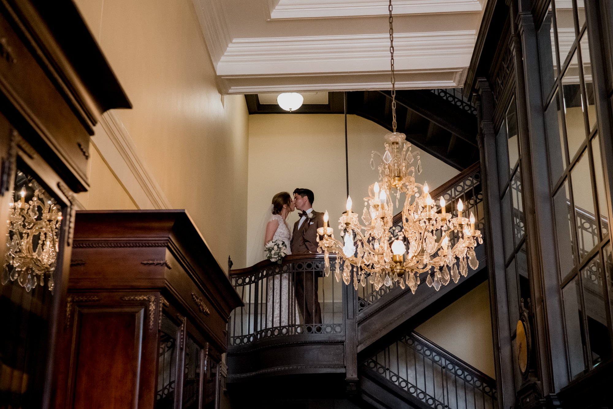 Bride and groom kissing on stairs with the golden chandelier. Wedding at Hotel Icon