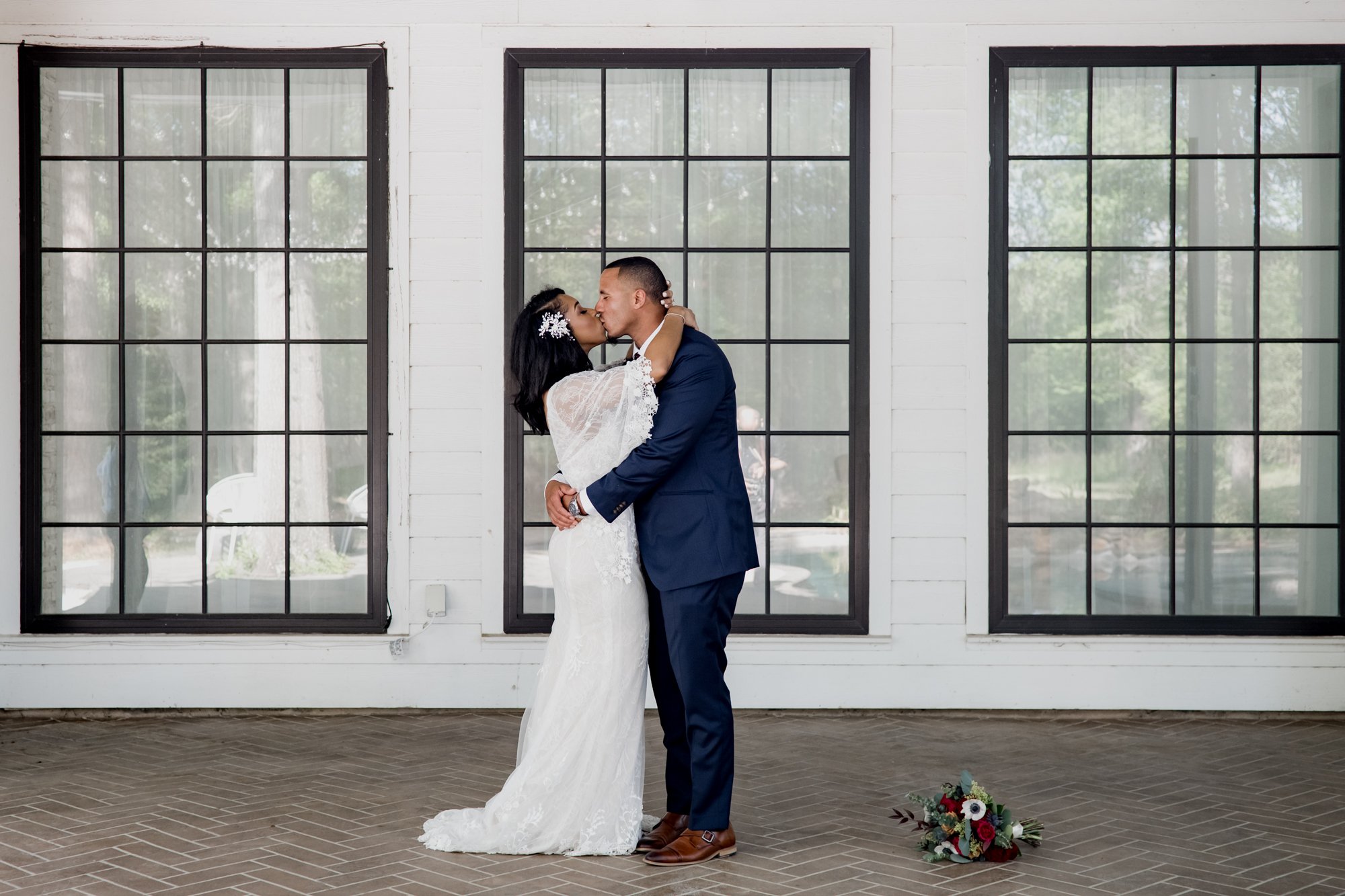 Bride and groom pose in front of the giant window. Wedding at The Oak Atelier
