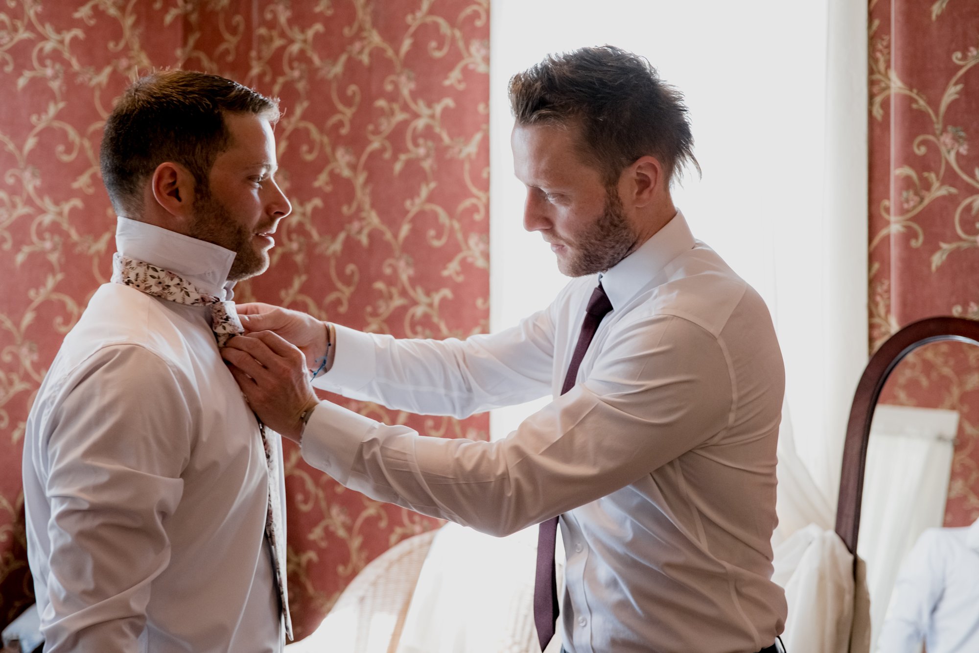 Best man helps groom with a tie. Groom getting ready. Wedding at Antique Rose Emporium