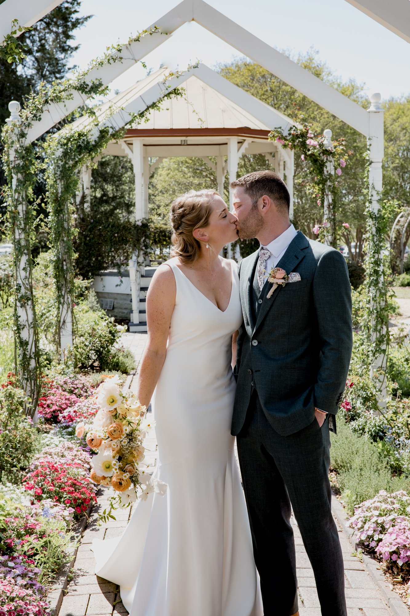 Bride and groom kiss under the arch in the flower garden. Wedding at Antique Rose Emporium