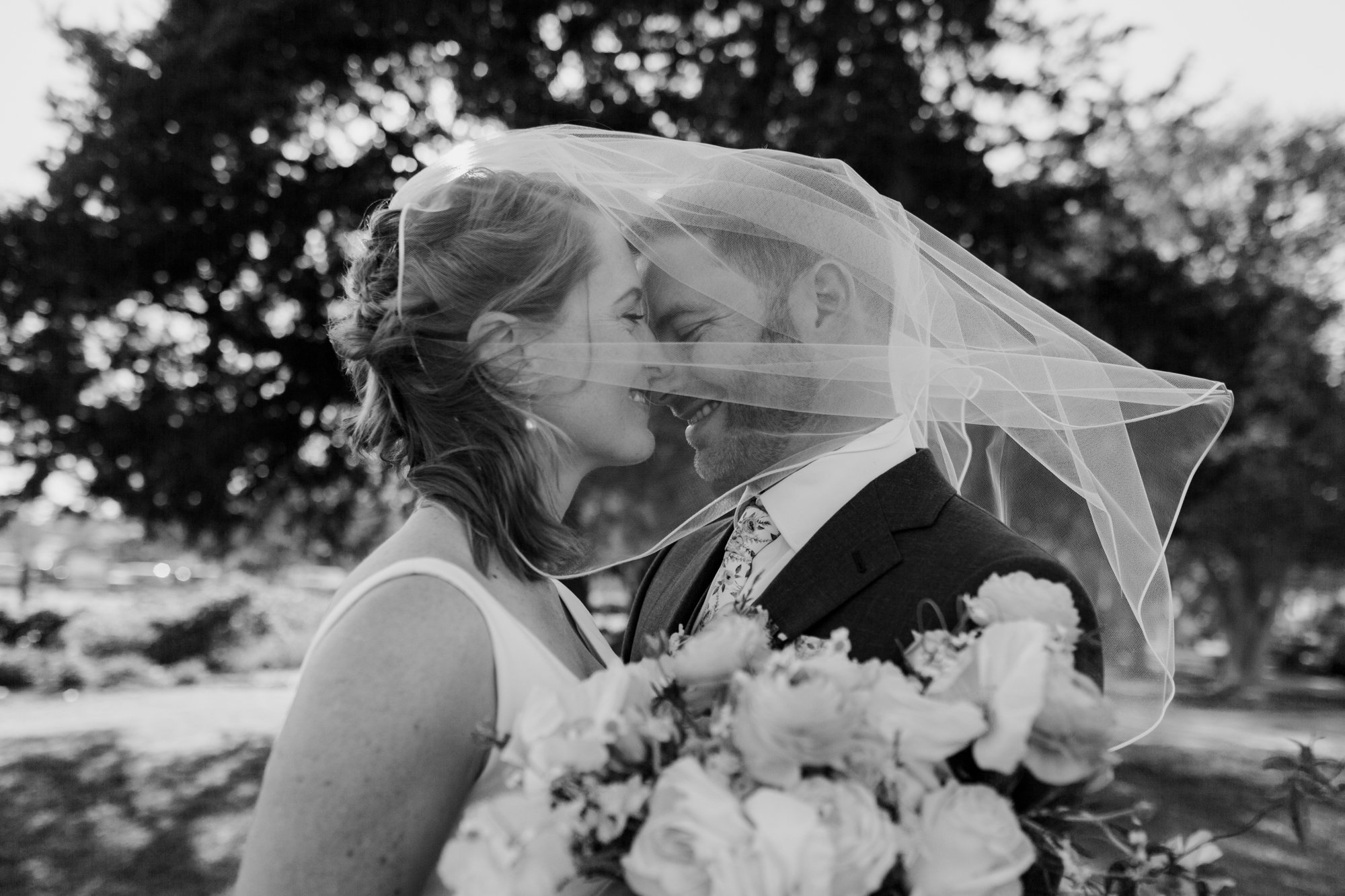 Bride and groom under veil kiss. Wedding at Antique Rose Emporium