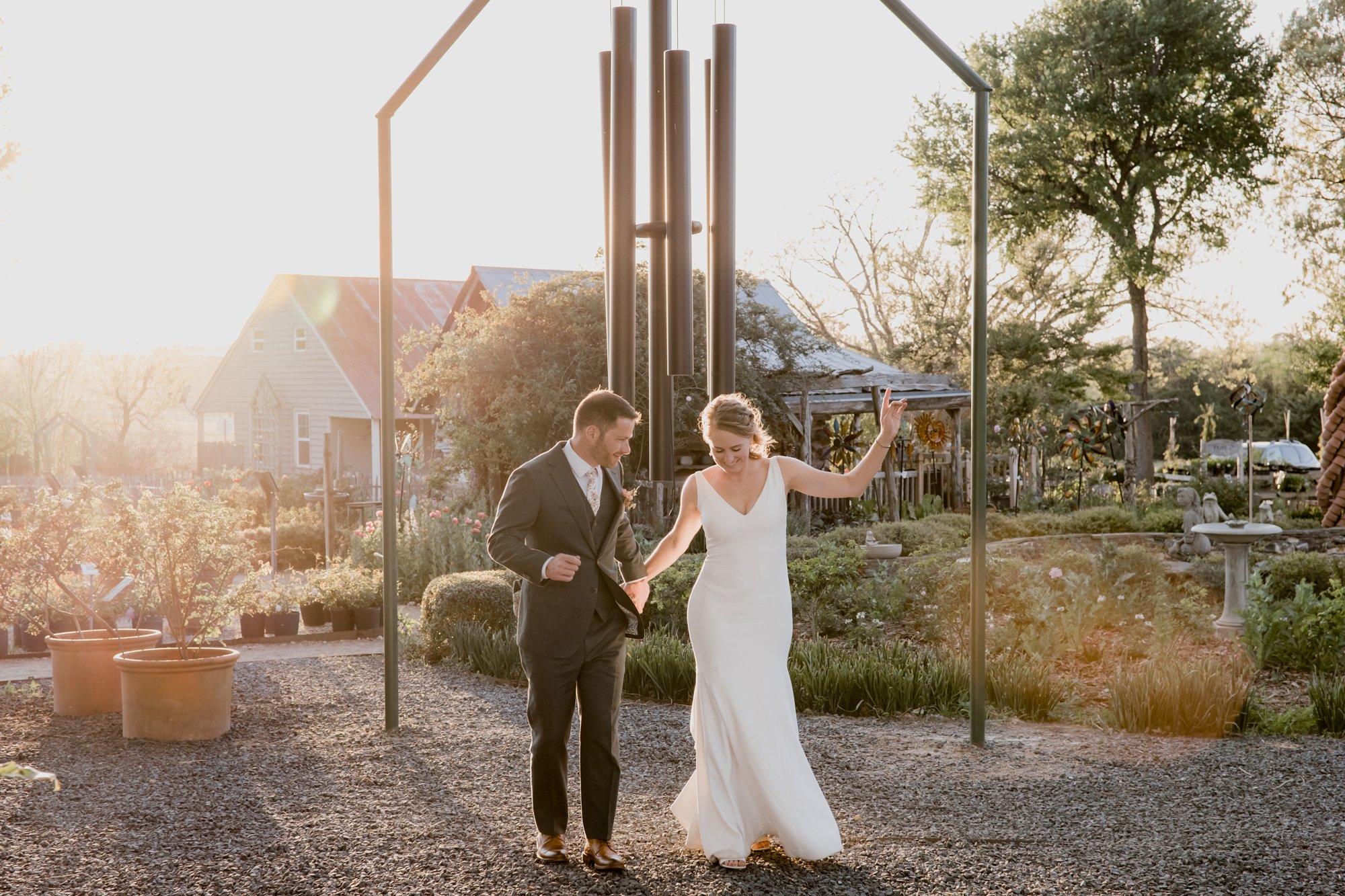 Bride and groom golden hour portraits dancing in a sunlight with a giant wind chime. Wedding at Antique Rose Emporium