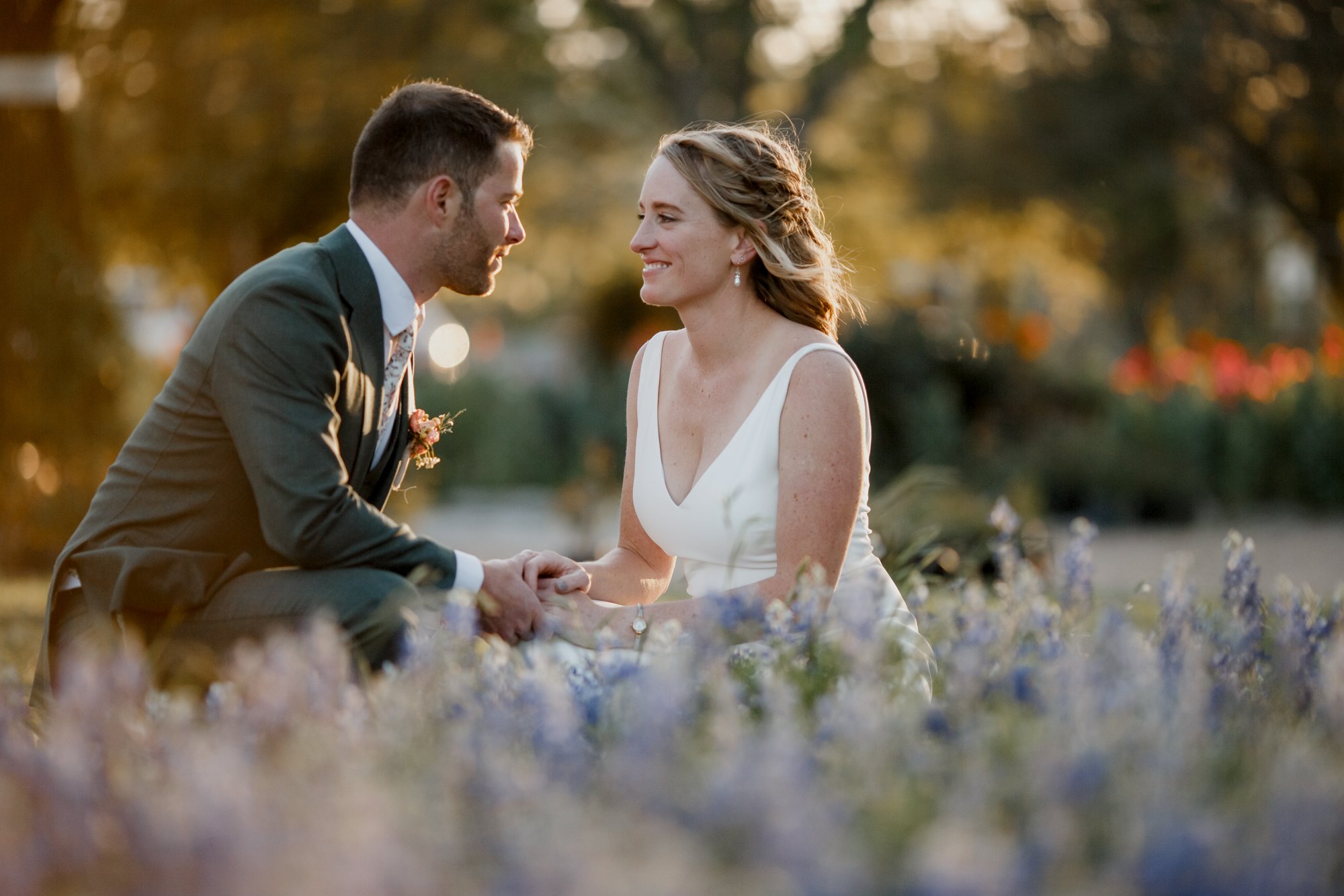 Bride and groom sitting in a field of blue bonnets golden hour. Wedding at Antique Rose Emporium
