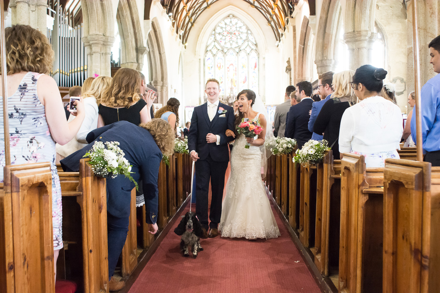 the bride, groom and their dog walk down the aisle at st mary's church plympton plymouth