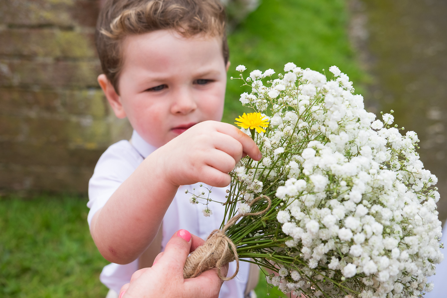 page boy picks a yellow flower for his mum and puts it into her bouquet outside st mary's church in woolacombe