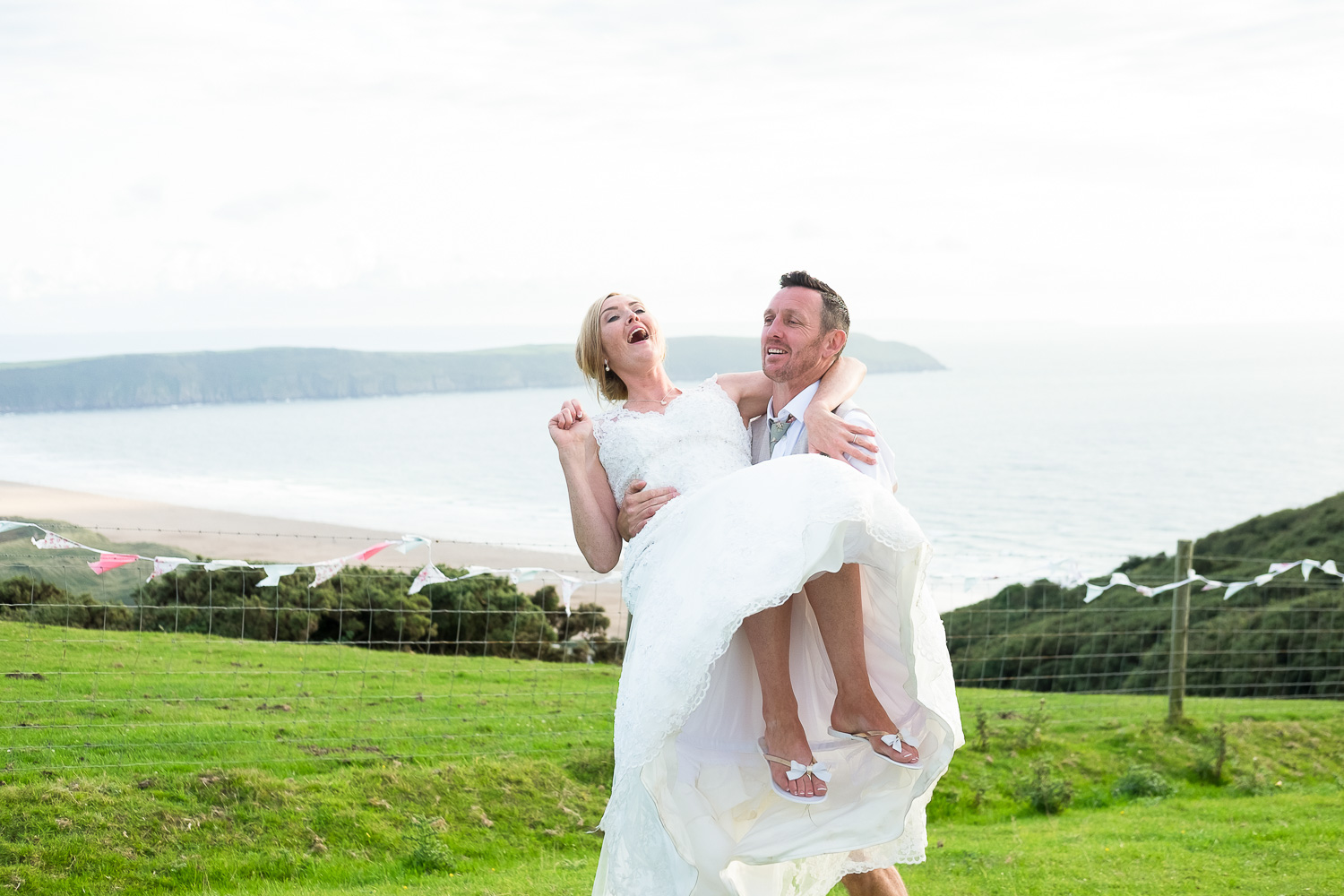 groom lifts up his bride with a beautiful woolacombe seaside view in the background