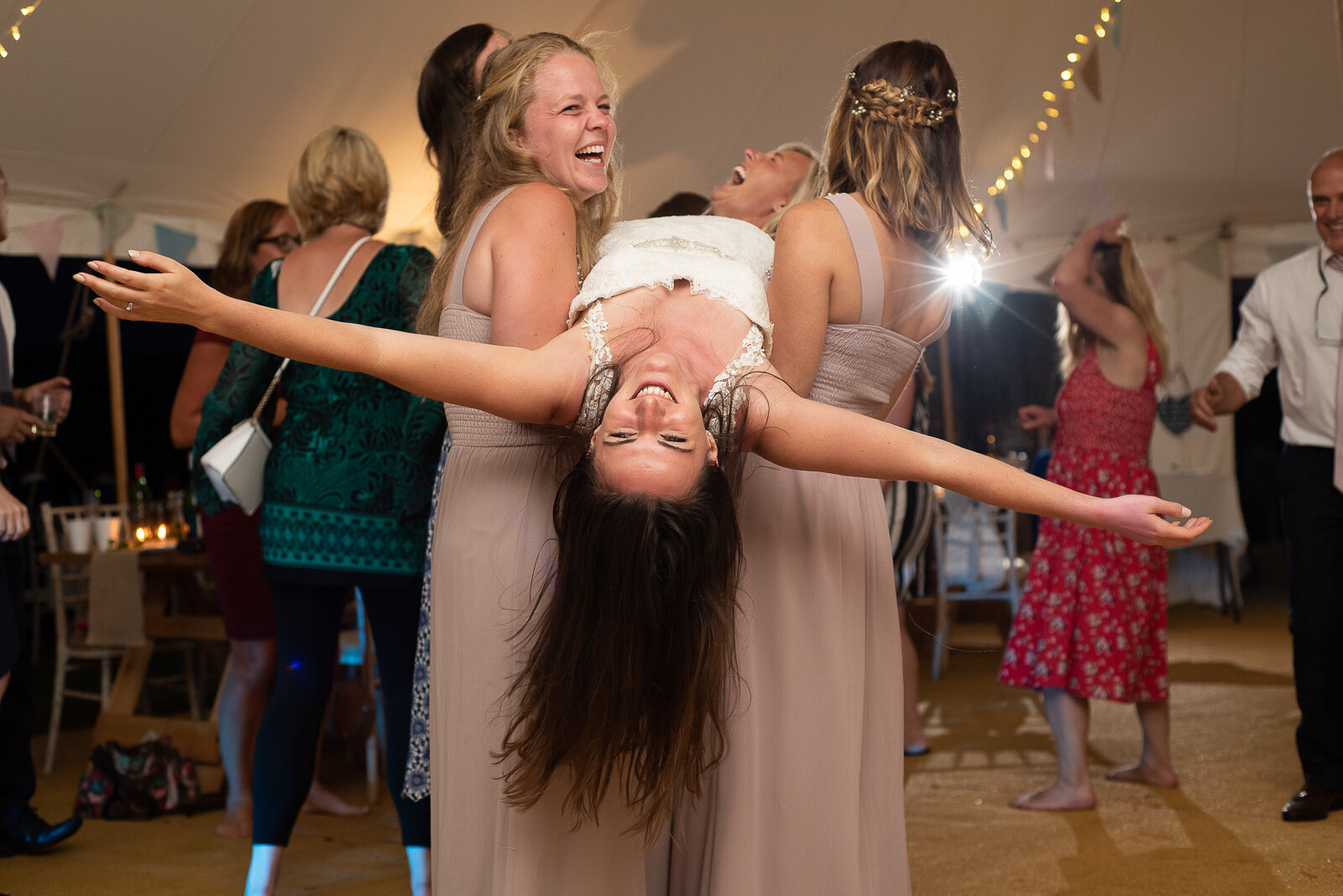 Bride+being+carried+by+friends+on+the+dancefloor+at+festival+style+wedding+in+cornwall.jpeg