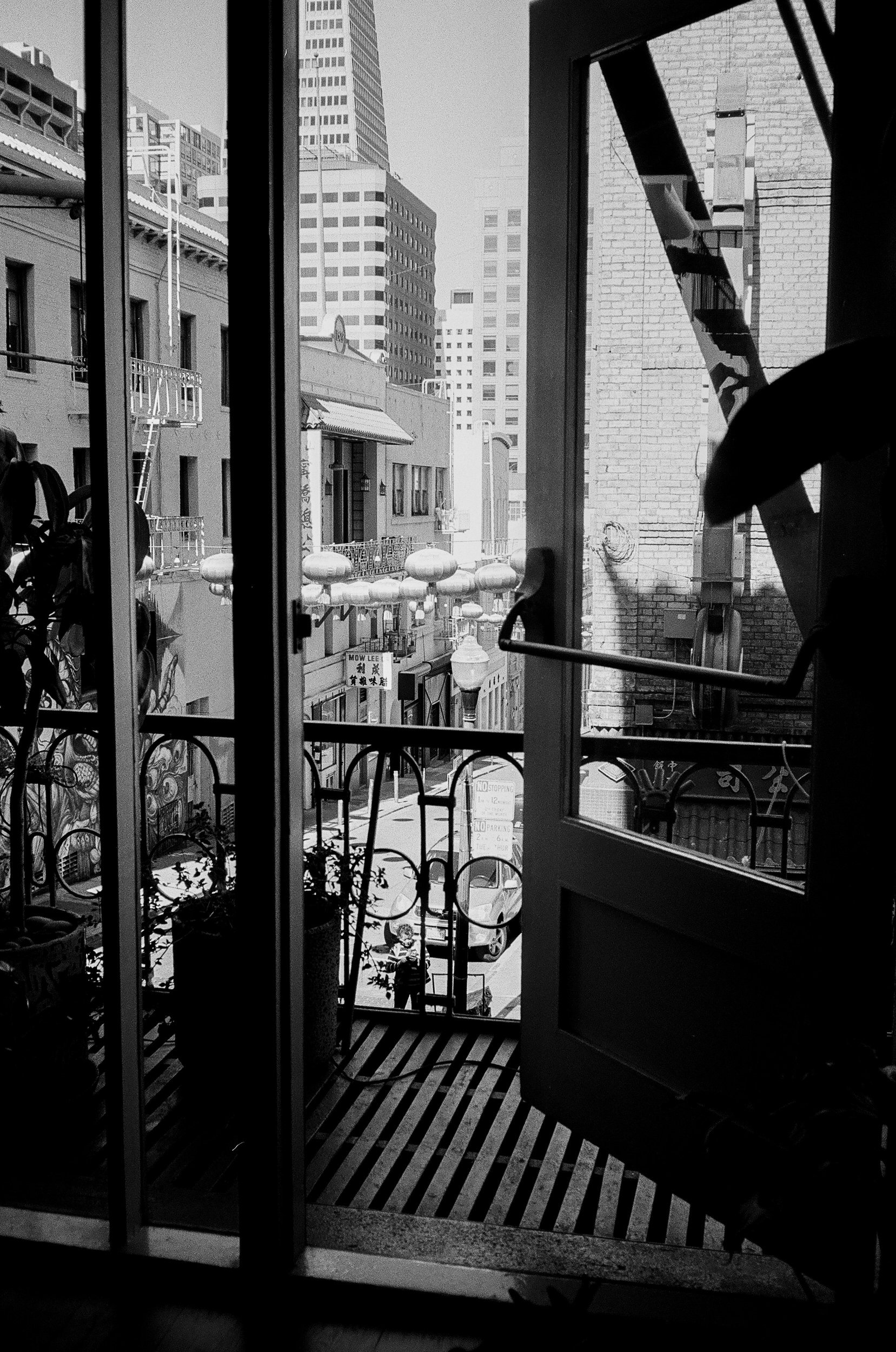 City street view through an open balcony door with buildings and street signs in the background.
