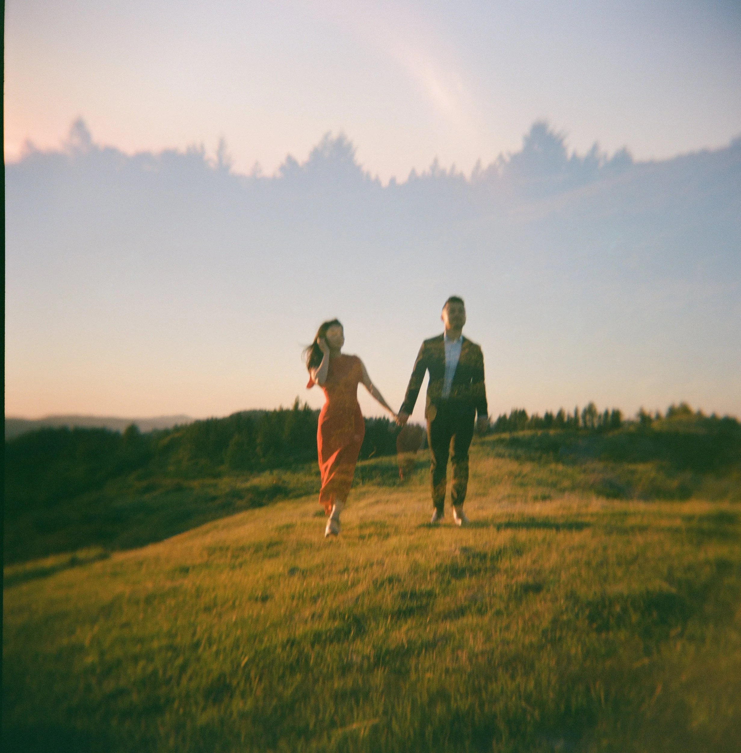 A couple walking hand in hand across a grassy field at sunset.