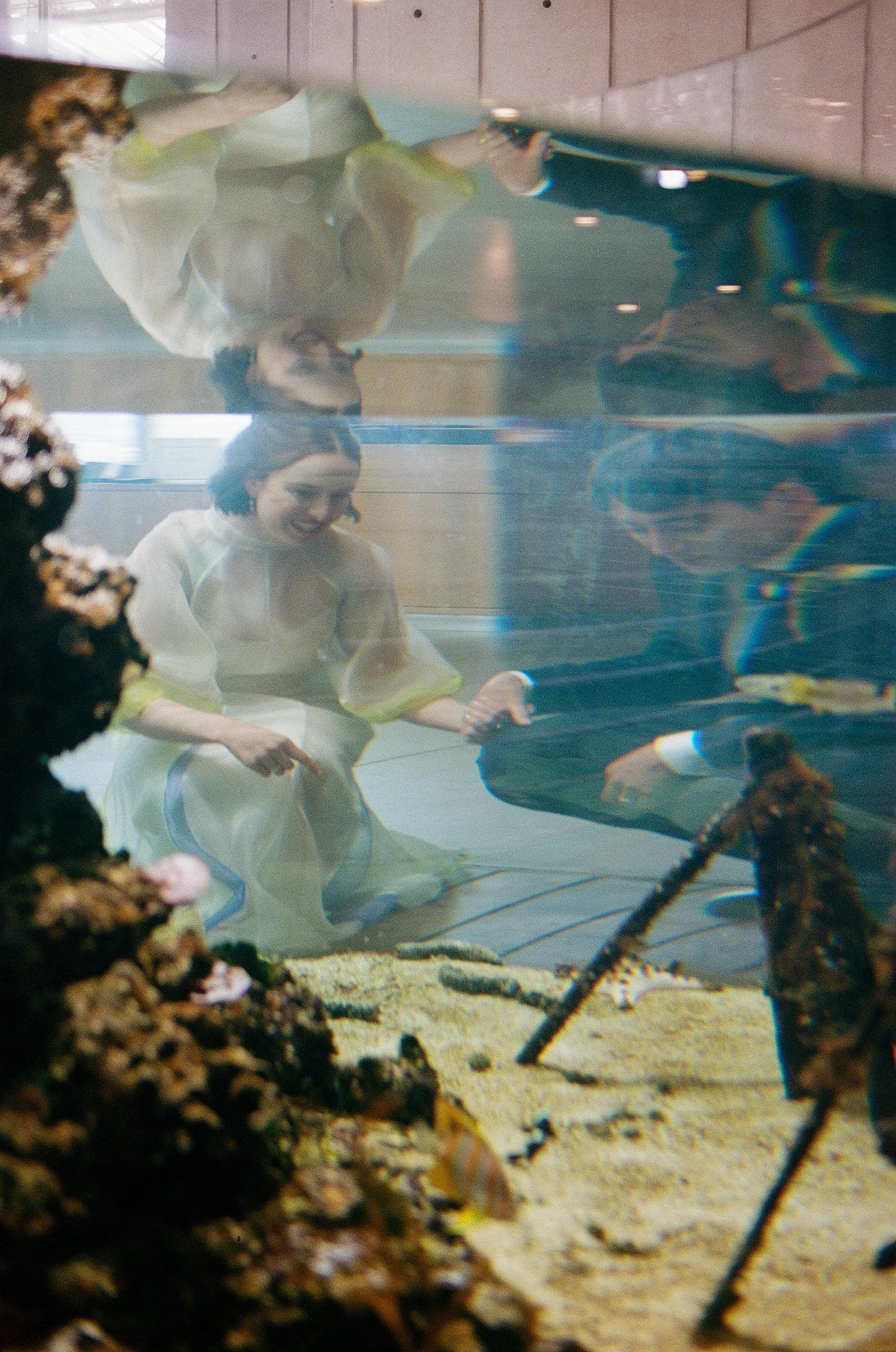 A woman playing piano in an indoor space, seen through a glass or water with reflections and distortions.