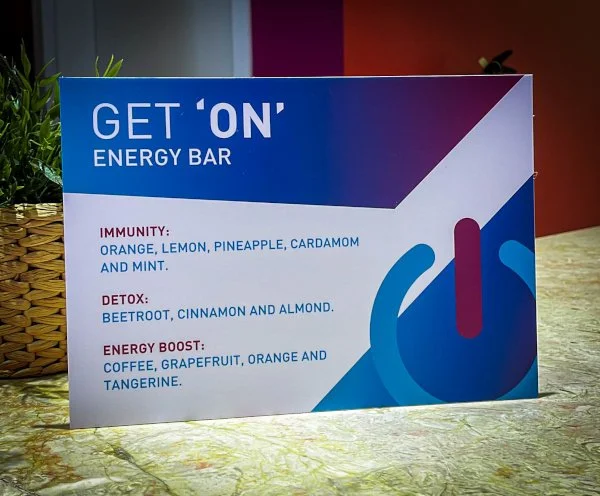 Cartaz promocional da barra de energia 'Get 'On' com informações sobre ingredientes e benefícios, incluindo imunidade, detox e aumento de energia.