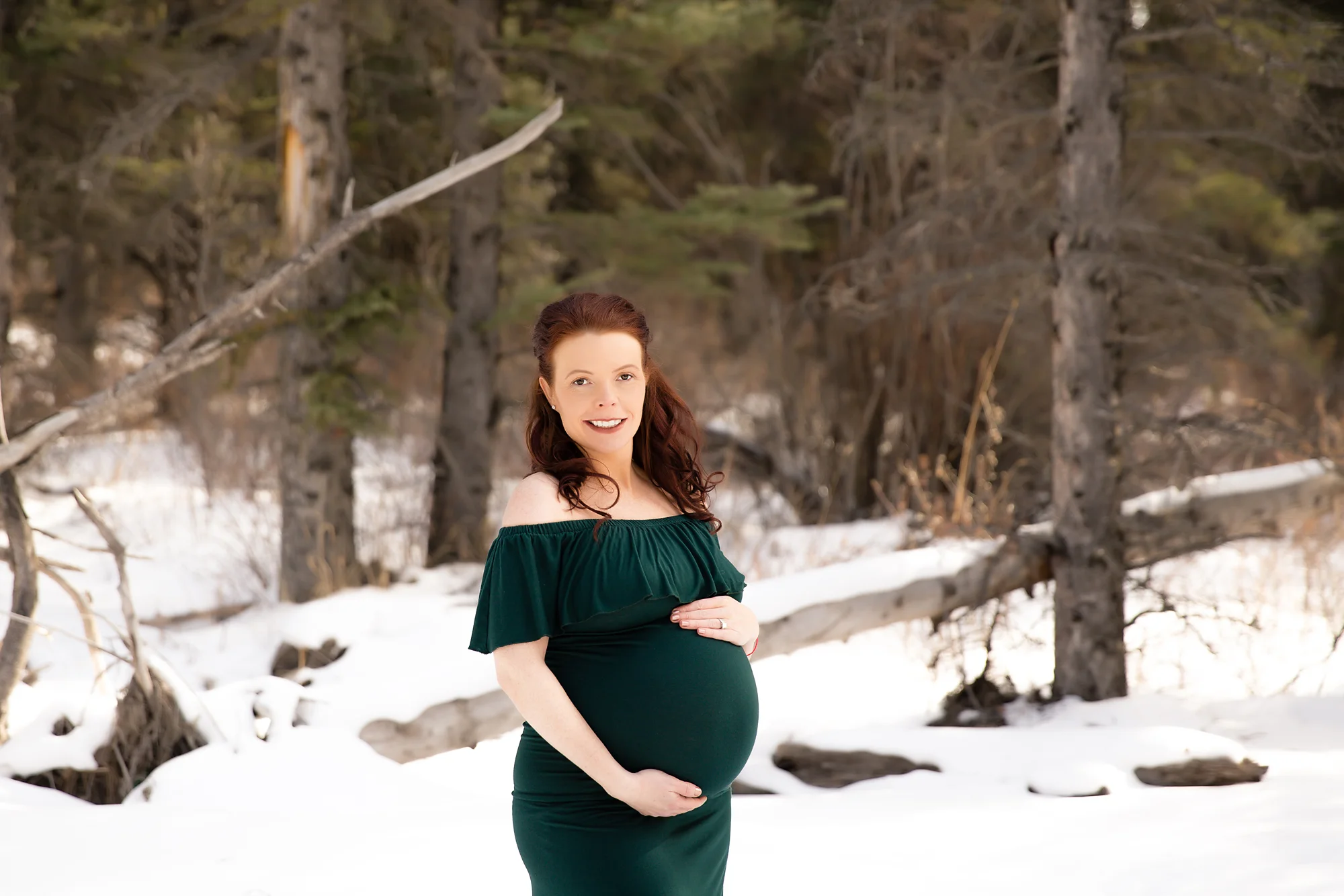 Mom-to-be wearing a green gown in the forest, looking at the camera and smiling. Calgary maternity photographer - Milashka Photography