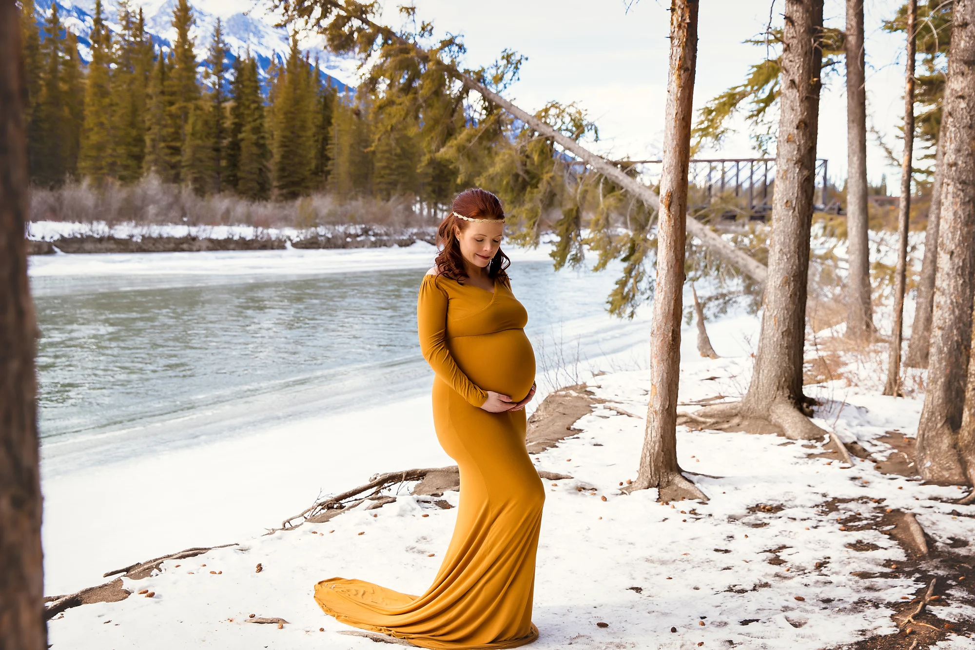 Mountain Maternity Session in Kananaskis, Alberta. Mother-to-be is wearing a mustard gown and is standing in front of a river .