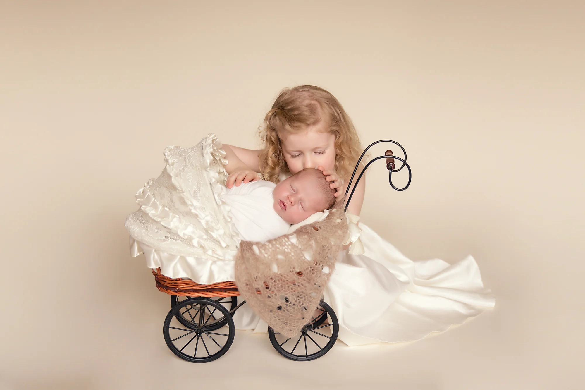 Big sister is kissing her newborn brother in a stroller. Calgary Newborn and Baby photographer - Milashka Photography.