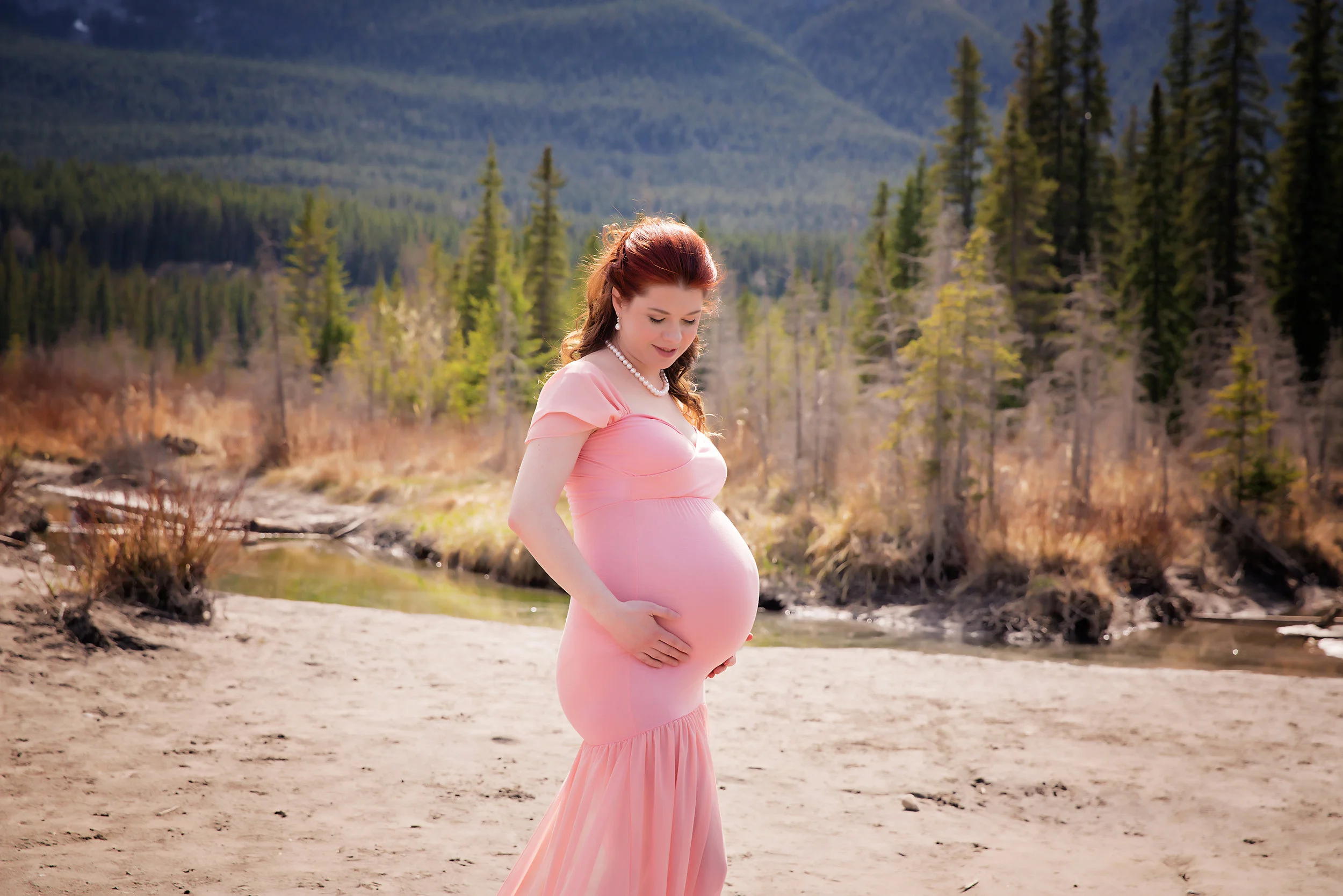 Mama to be is posing in a beautiful dusty pink dress in the mountains. Calgary maternity photographer - Milashka Photography