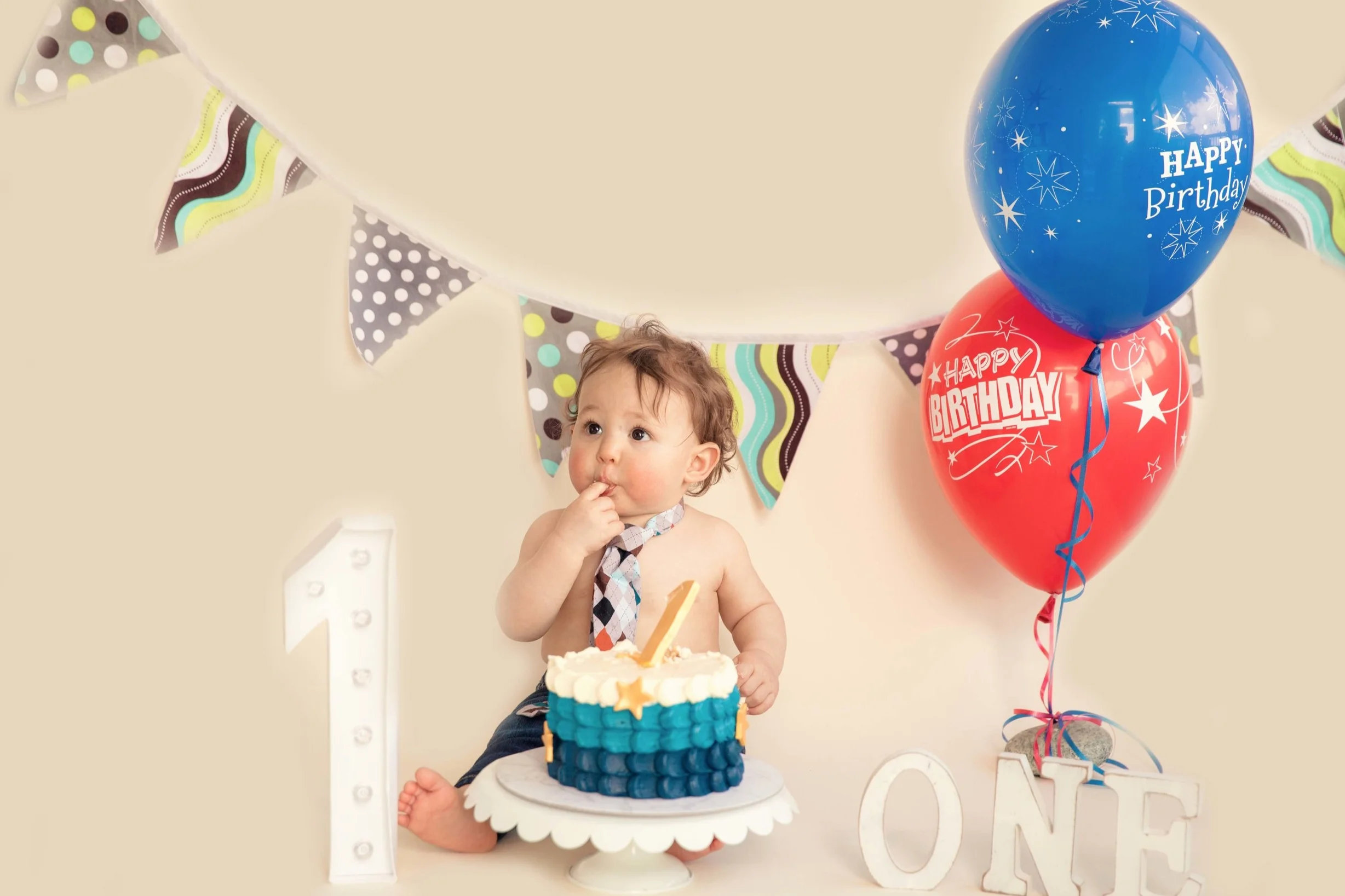 Baby boy just tried his birthday cake for the first time and is licking his finger. Cakesmash photographer in Calgary, Alberta