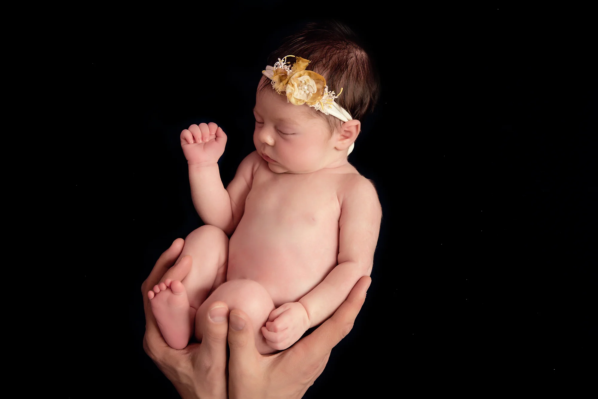 Newborn baby girl photoshoot idea. Calgary and Airdrie Newborn Photographer - Milashka Photography. Baby girl is posed on a beanbag with her daddy’s hands holding her.