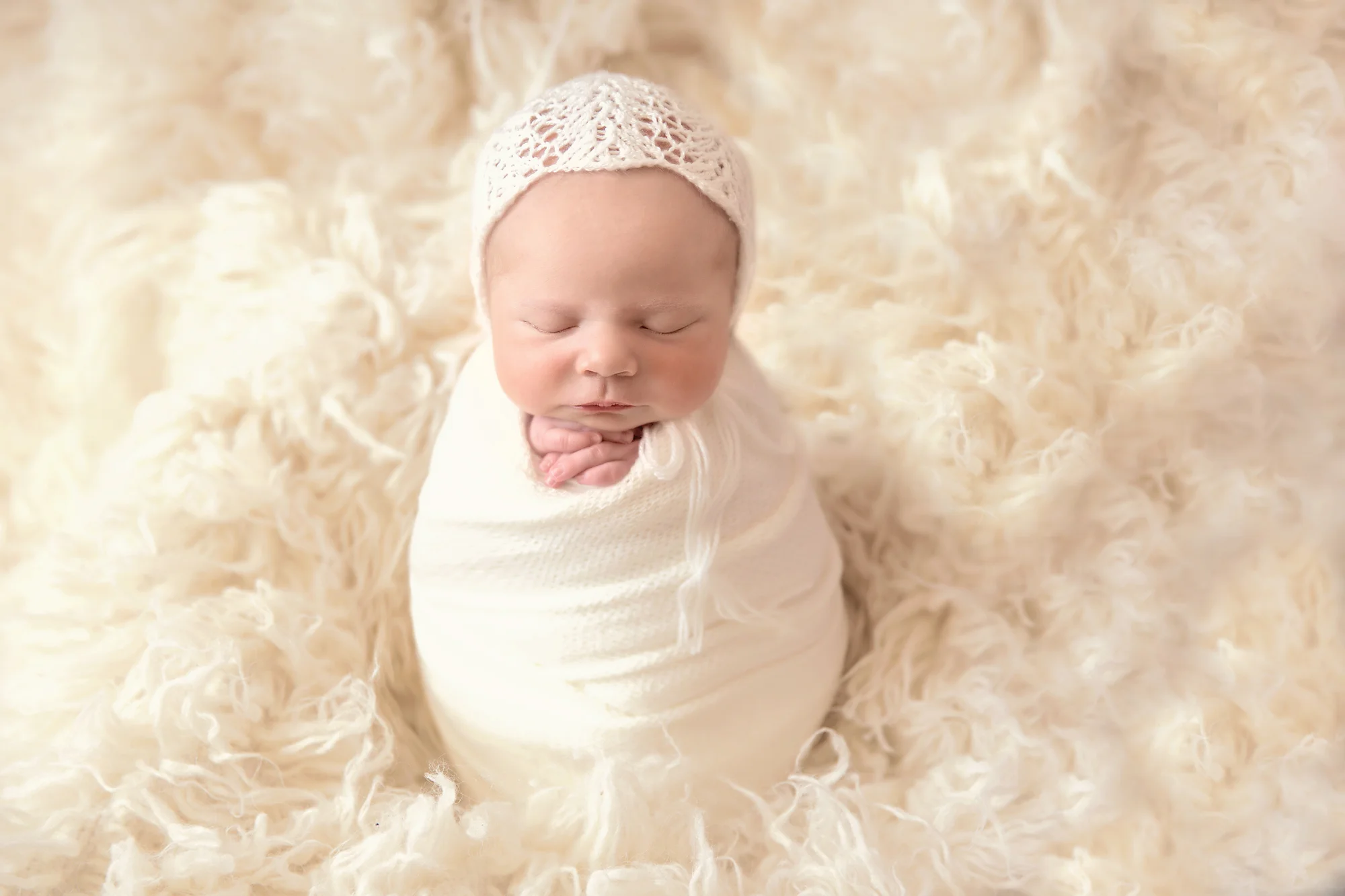 Newborn baby girl wrapped in a white wrap, wearing a white bonnet and is posed in a “potato sack” pose on a beanbag. Newborn Photoshoot inspiration ideas. Calgary and Airdrie, Alberta Newborn and Baby photographer - Milashka Photography.