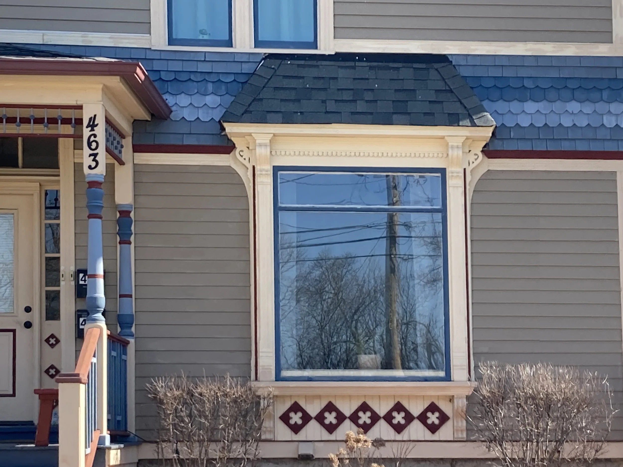 Victorian-style house front with large bay window, blue trim, porch column numbered "463" and low shrubs.