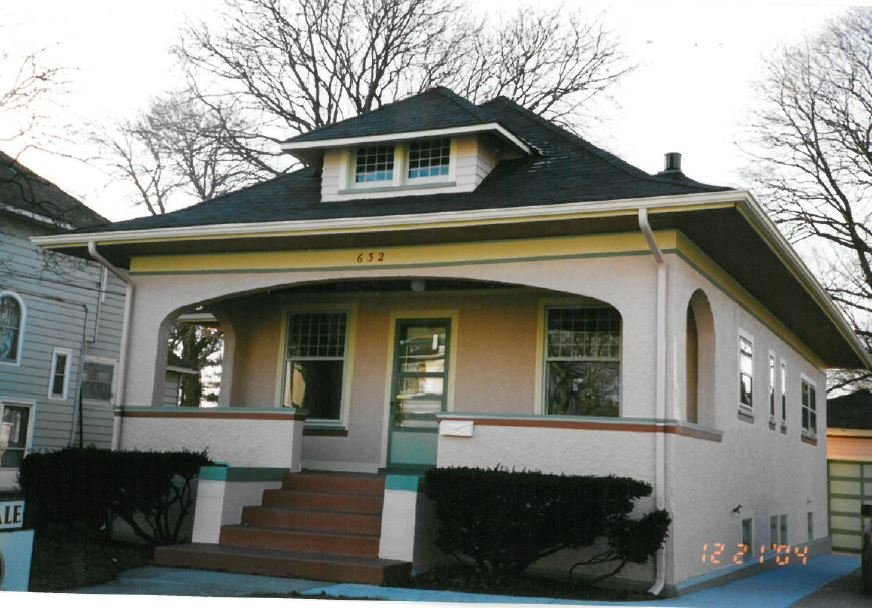 Front view of a single-story Craftsman bungalow with a covered porch, steps leading to a green door, stucco exterior, dormer window, and house number "632" above the porch.