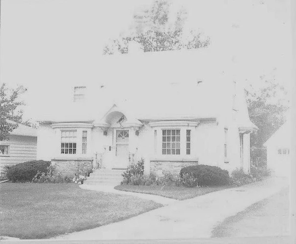 Front view of a two-story suburban house with front steps, shrubs and a curved driveway.