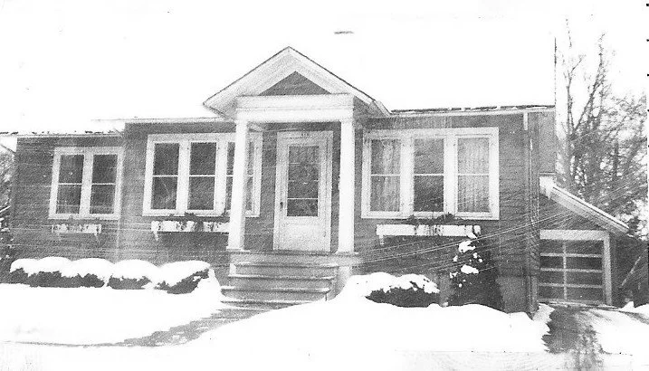 Front single-story bungalow with a columned porch, snow-covered yard and driveway, and attached garage on the right.