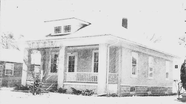 Front view of a single-story bungalow with a covered wraparound porch and snow on the ground.