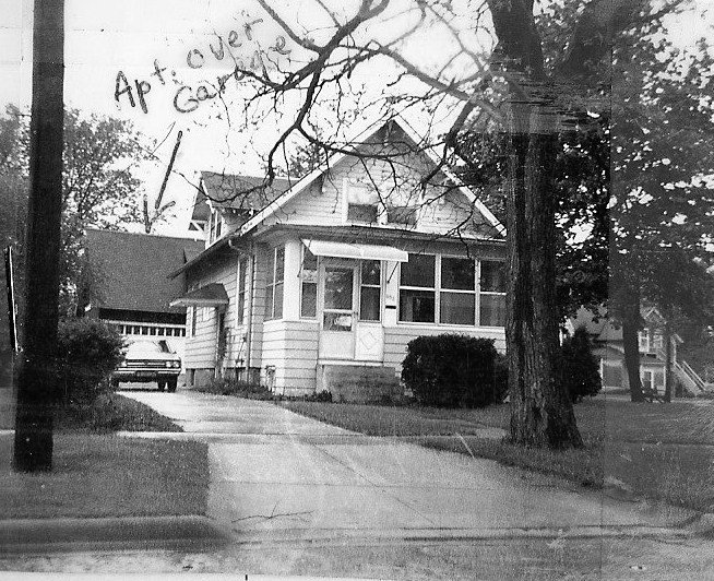 Black-and-white photo of a small bungalow with enclosed front porch, driveway and parked car; handwritten arrow and note "Apt. over garage" point to the left.