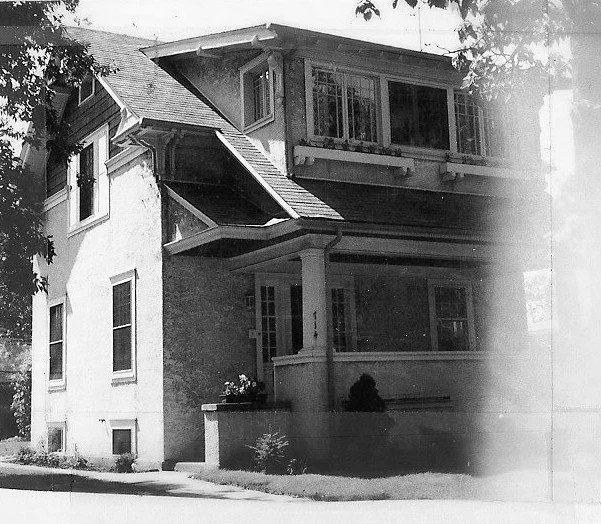 Black-and-white photo of a two-story Craftsman-style house with a covered porch and enclosed upper sunroom.