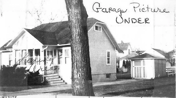 Black-and-white photo of a small bungalow with a front porch, large tree in the foreground, and a detached garage; handwritten notes visible.