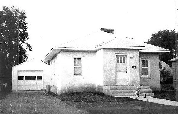 One-story stucco house with front steps, a child's tricycle on the walkway, and a detached garage to the left.